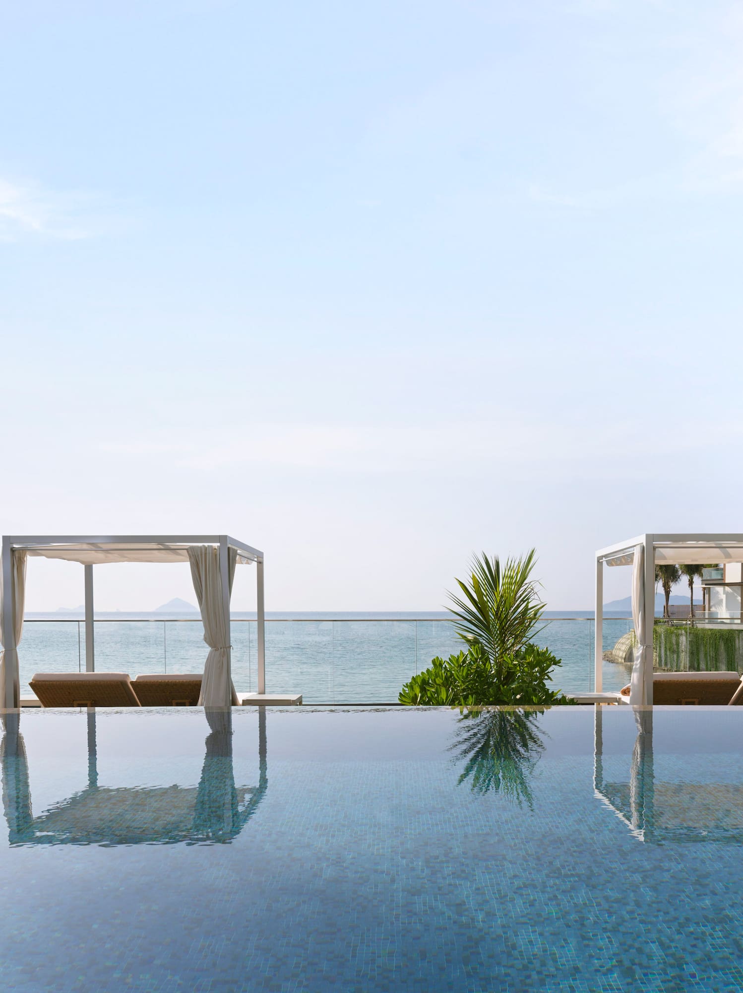 Luxury infinity pool overlooking ocean, white cabanas, palm trees.