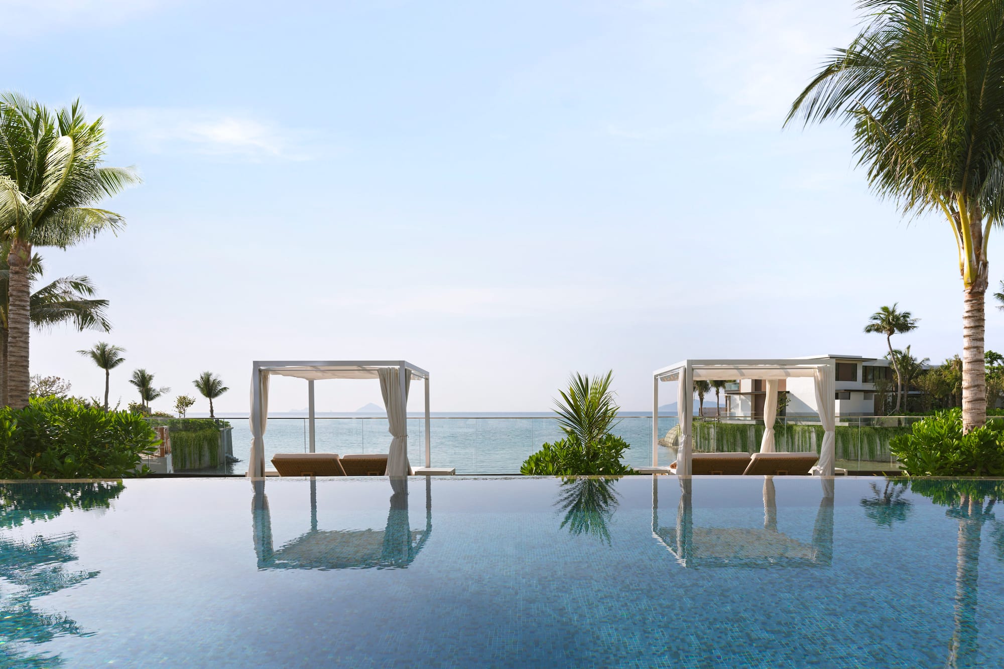 Luxury resort infinity pool with ocean view, white cabanas, and palm trees.