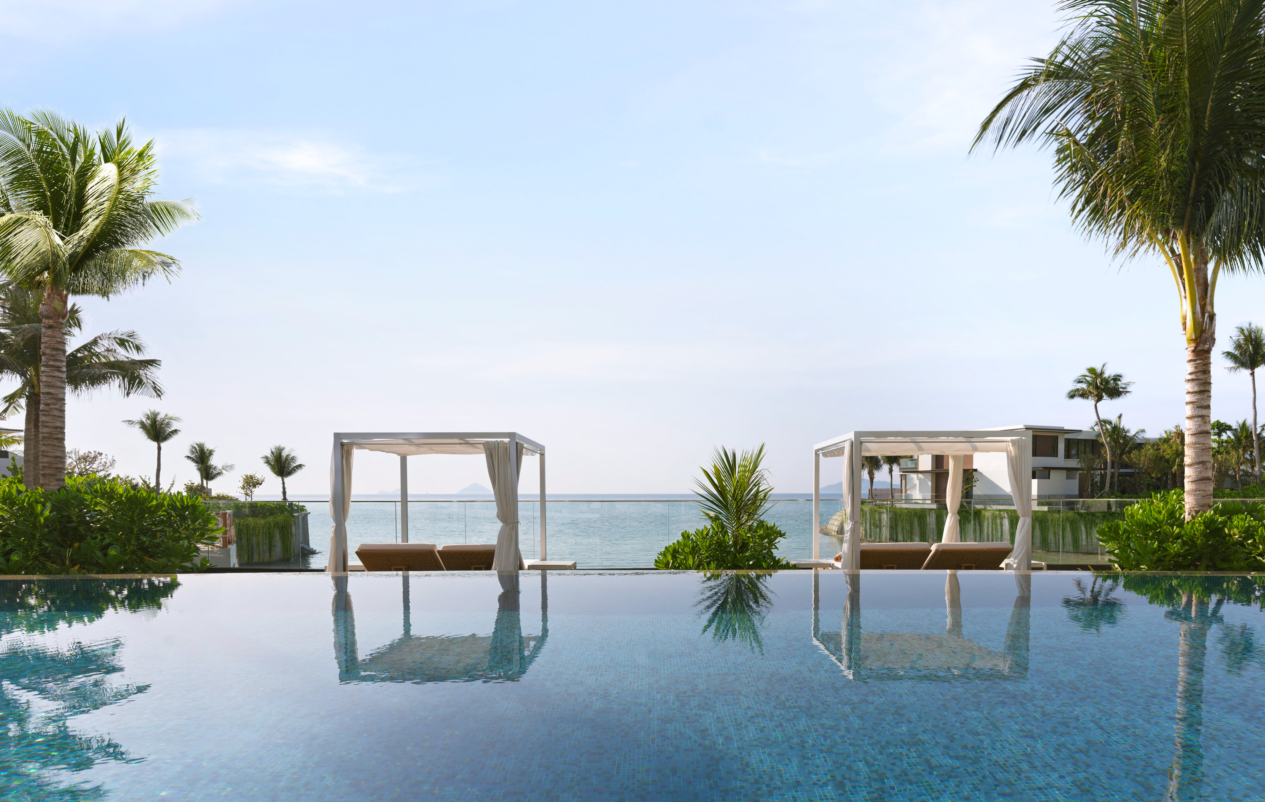 Luxury resort infinity pool with ocean view, white cabanas, and palm trees.