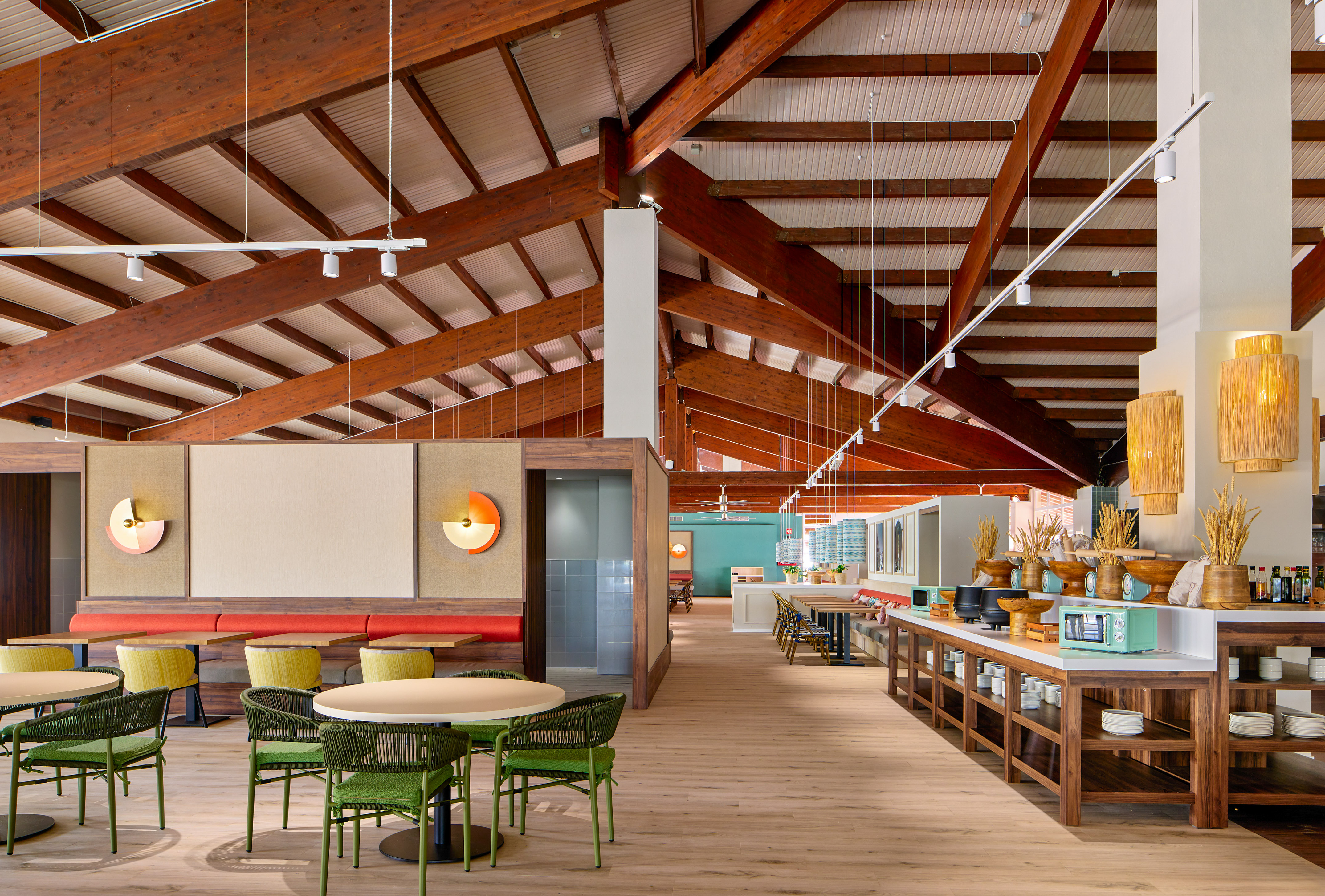 Modern restaurant with wooden ceiling beams, green chairs, and a long buffet.