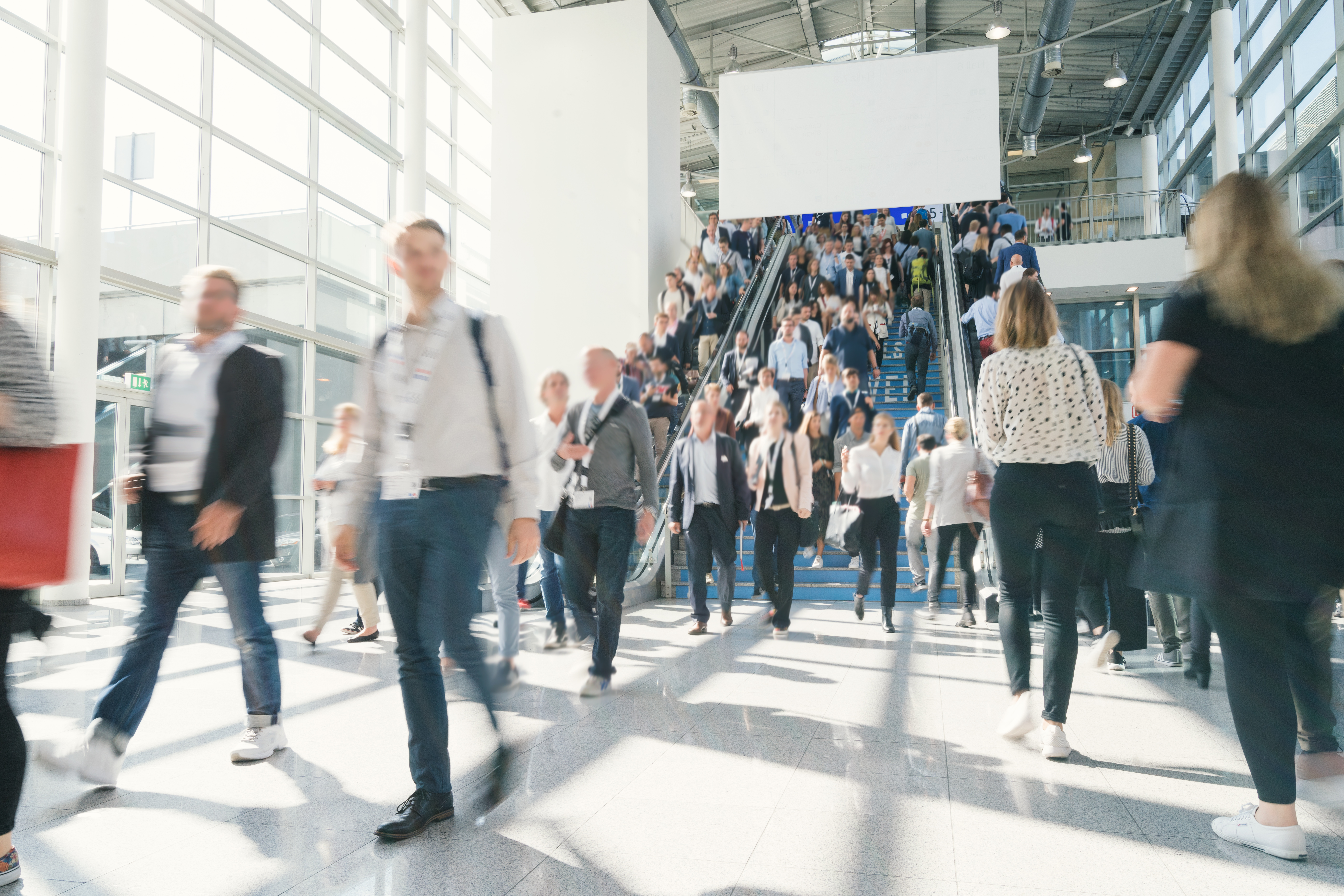 Crowd of professionals moving through a bright modern convention hall with stairs.