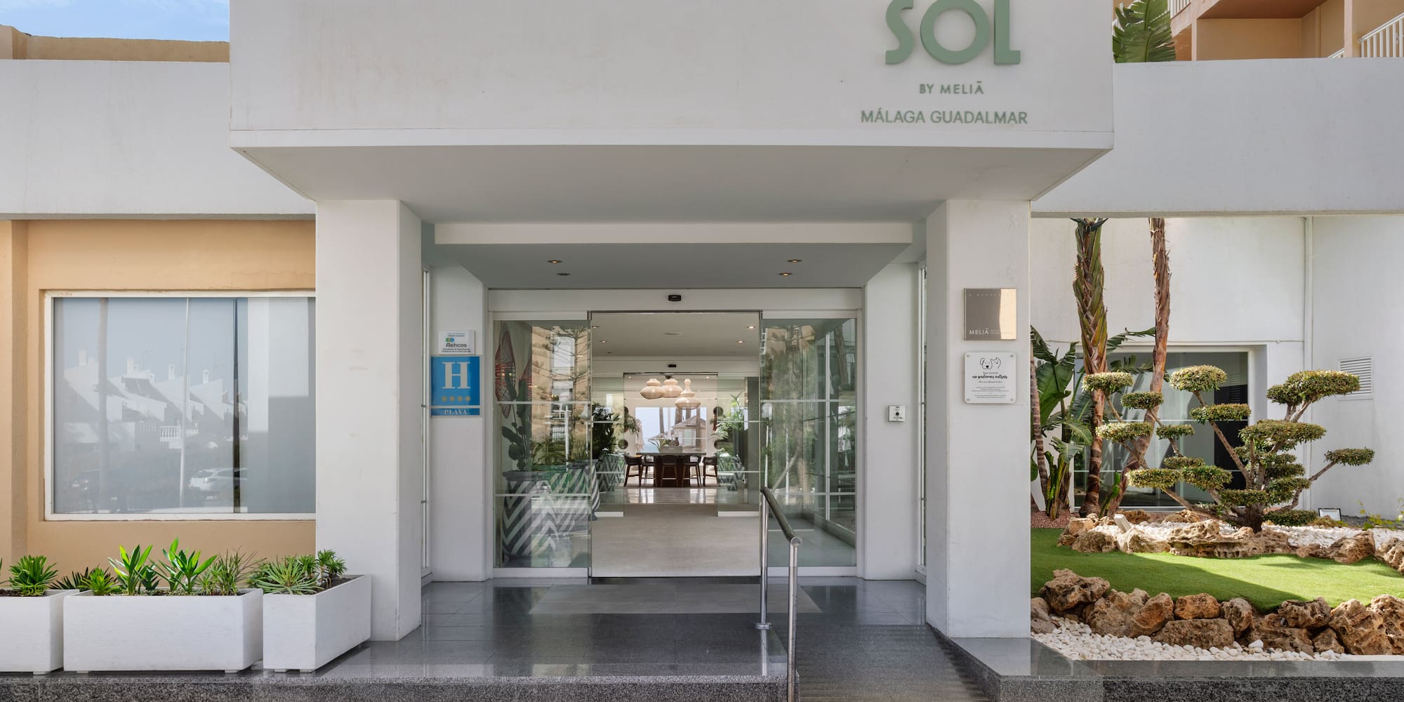 Modern Sol by Meliã Málaga Guadalmar hotel entrance, glass doors, lush plants.