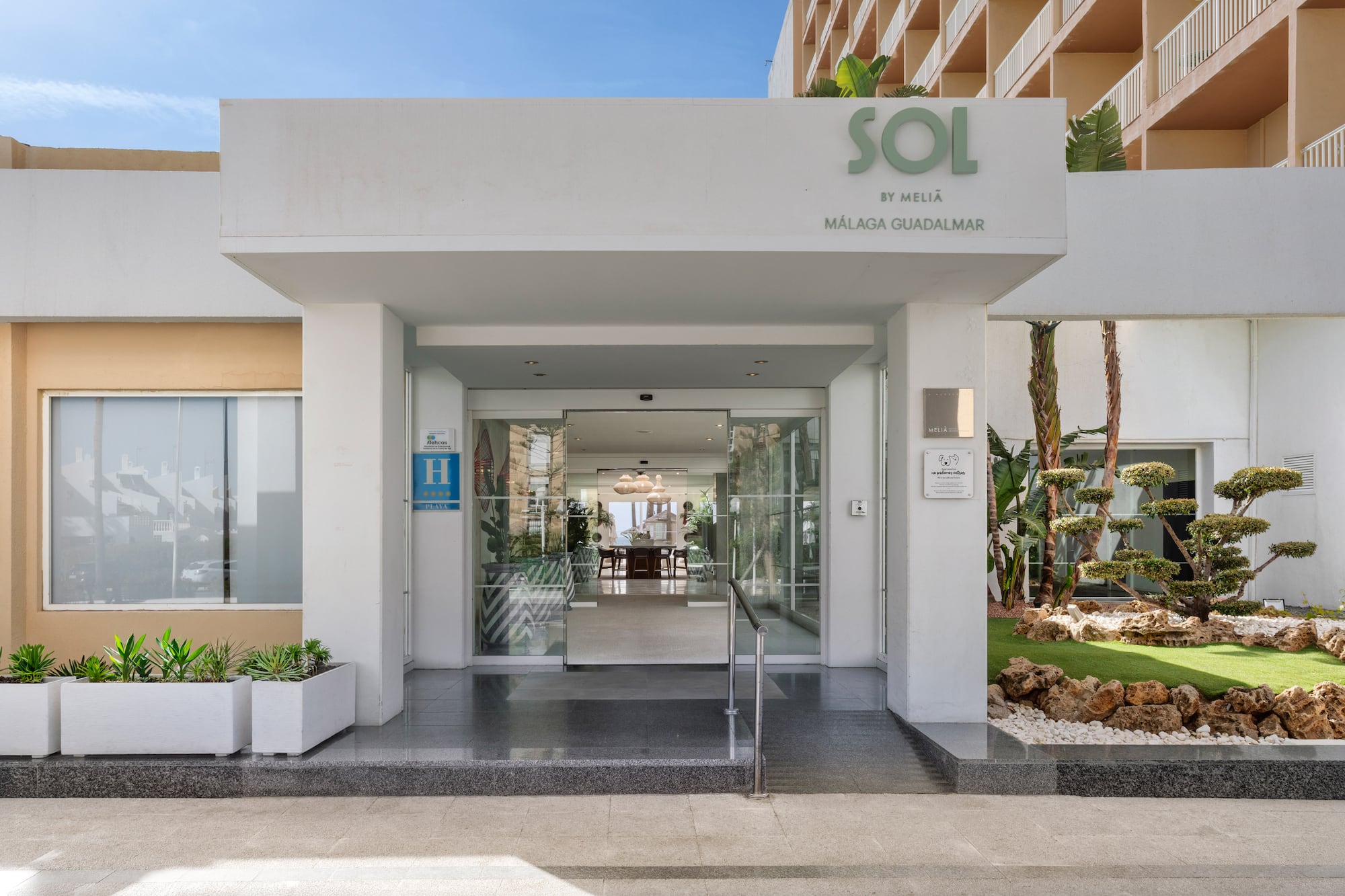 Modern Sol by Meliã Málaga Guadalmar hotel entrance, glass doors, lush plants.