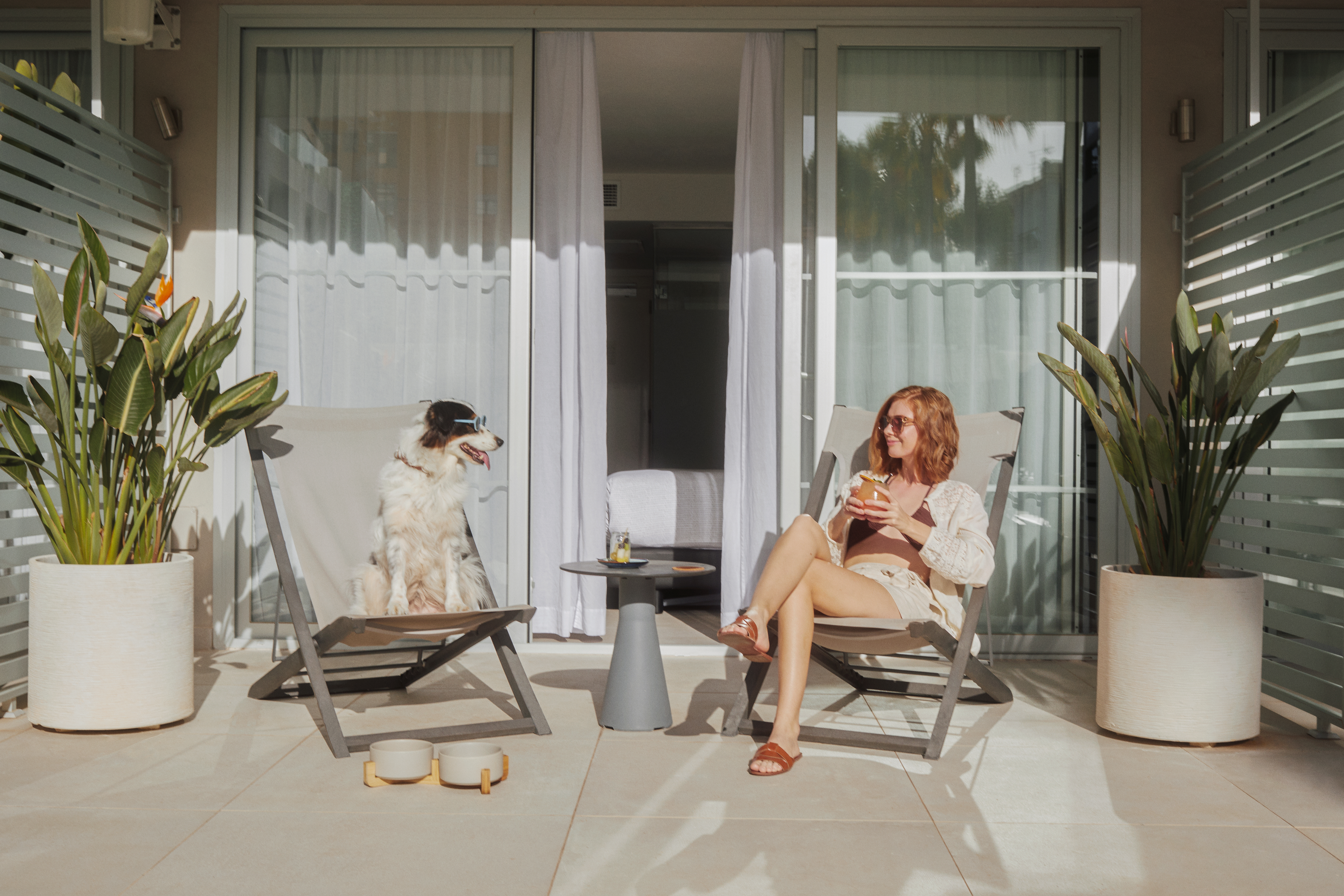 Woman and dog in sunglasses relaxing on sunny pet-friendly balcony.