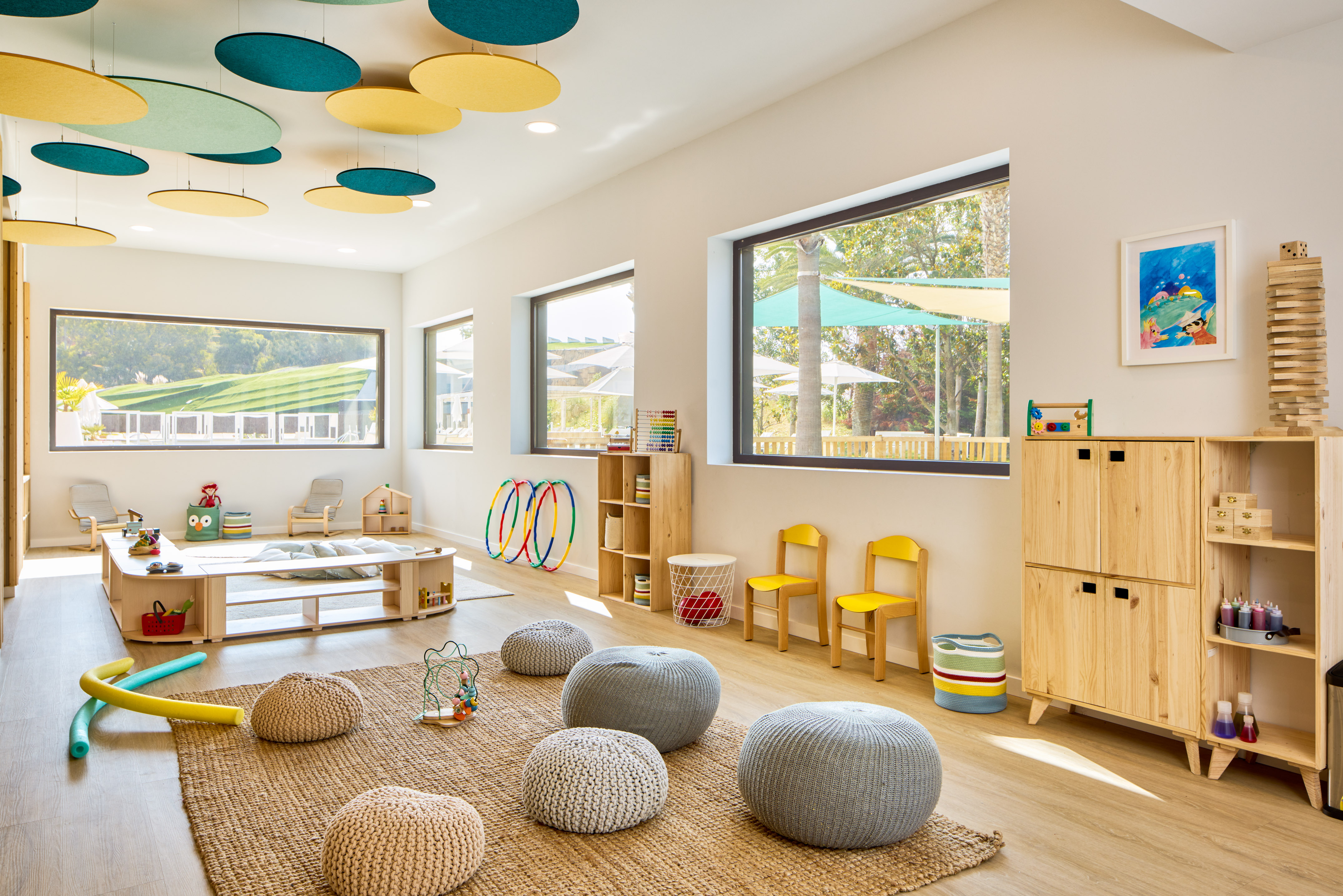 Bright children's playroom with colorful ceiling, wooden furniture, and soft poufs.