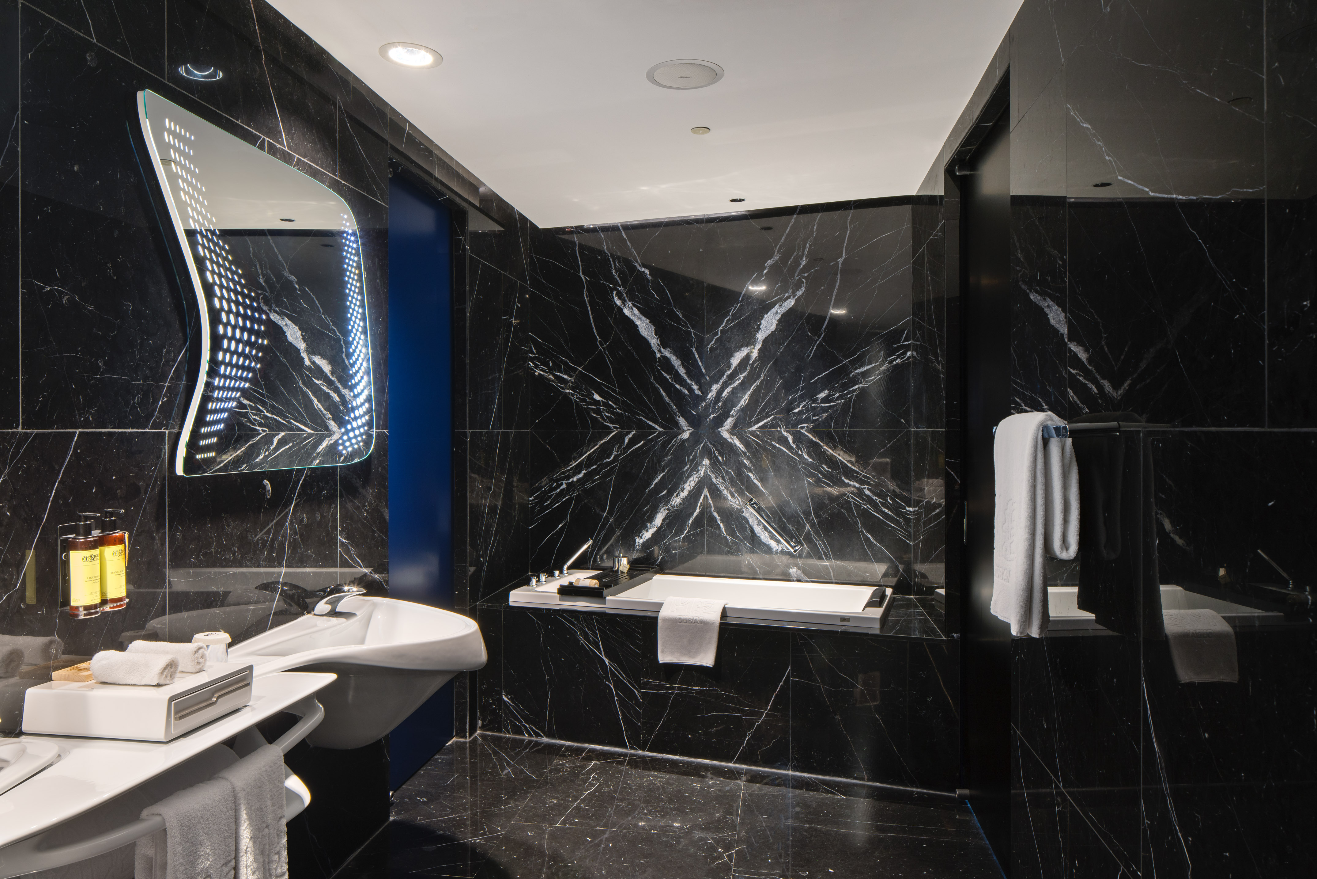 Modern black marble bathroom with illuminated mirror, white sink, and bathtub.