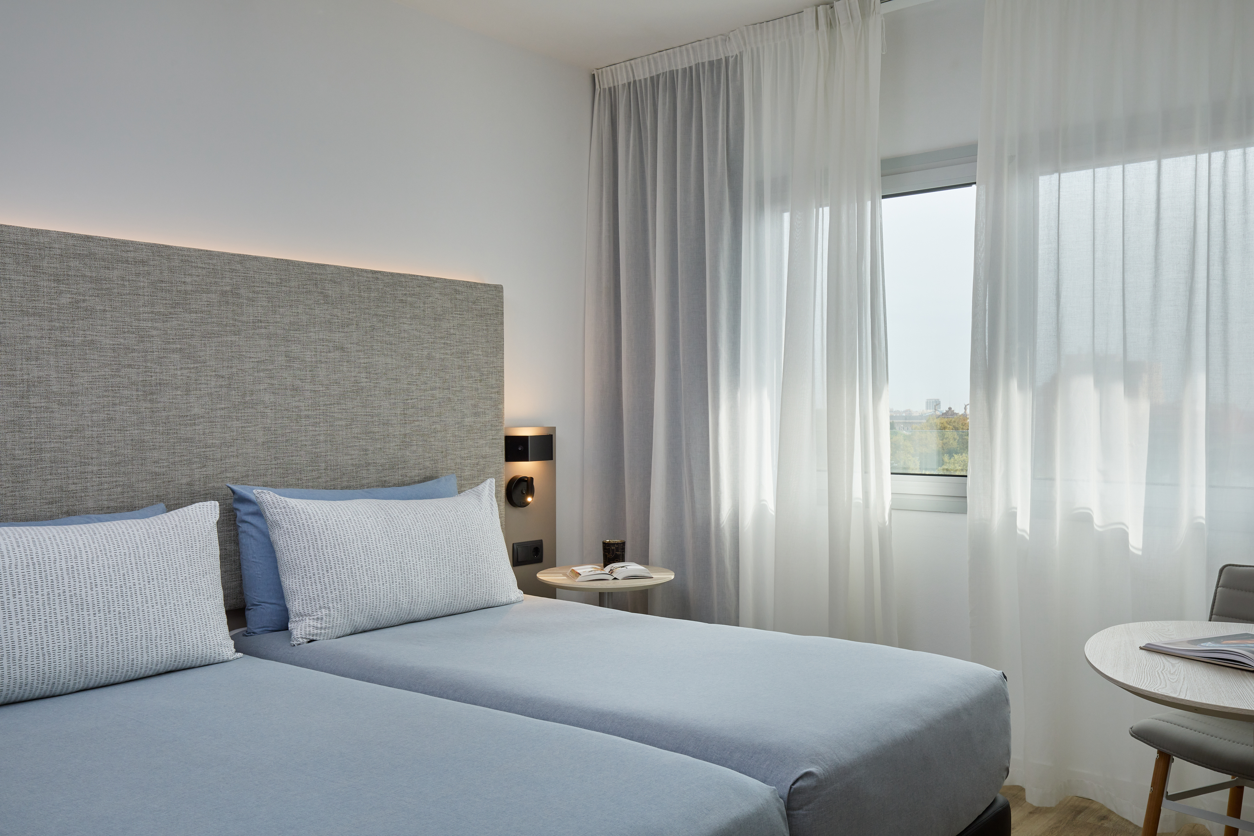 Modern hotel room with two twin beds, neutral decor, and bright window.
