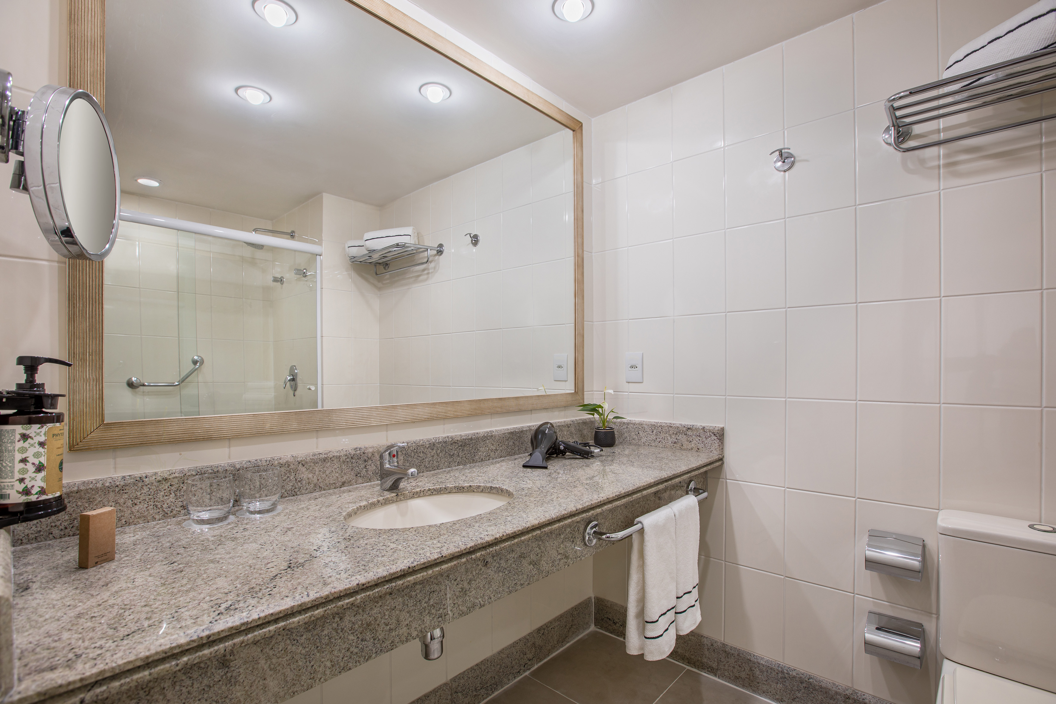 Modern hotel bathroom with granite vanity, sink, large mirror, and tiled walls.
