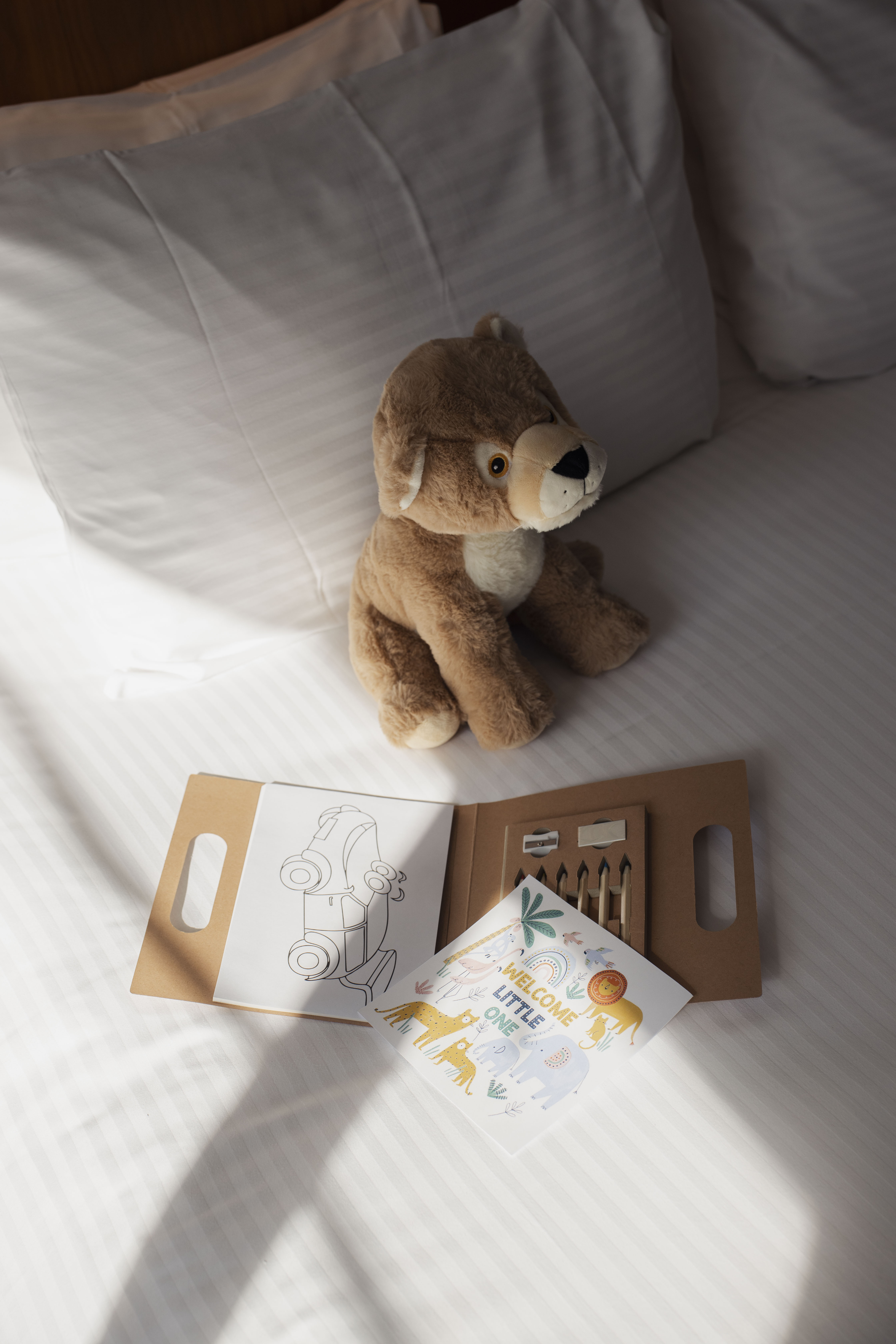 New baby welcome gift with plush lion, coloring book on hotel bed.