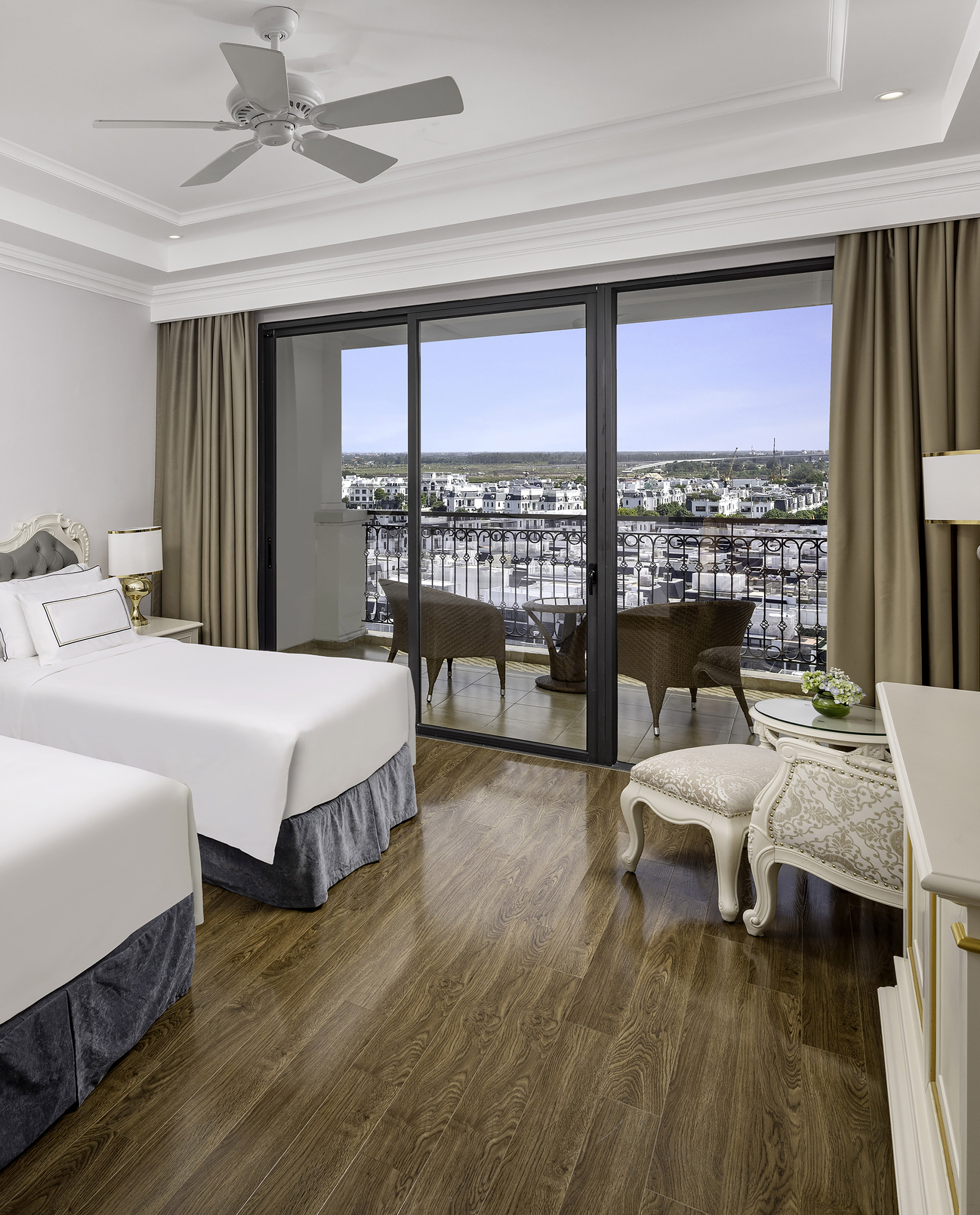 Twin bedroom with balcony, city view, wooden floor, and outdoor seating.