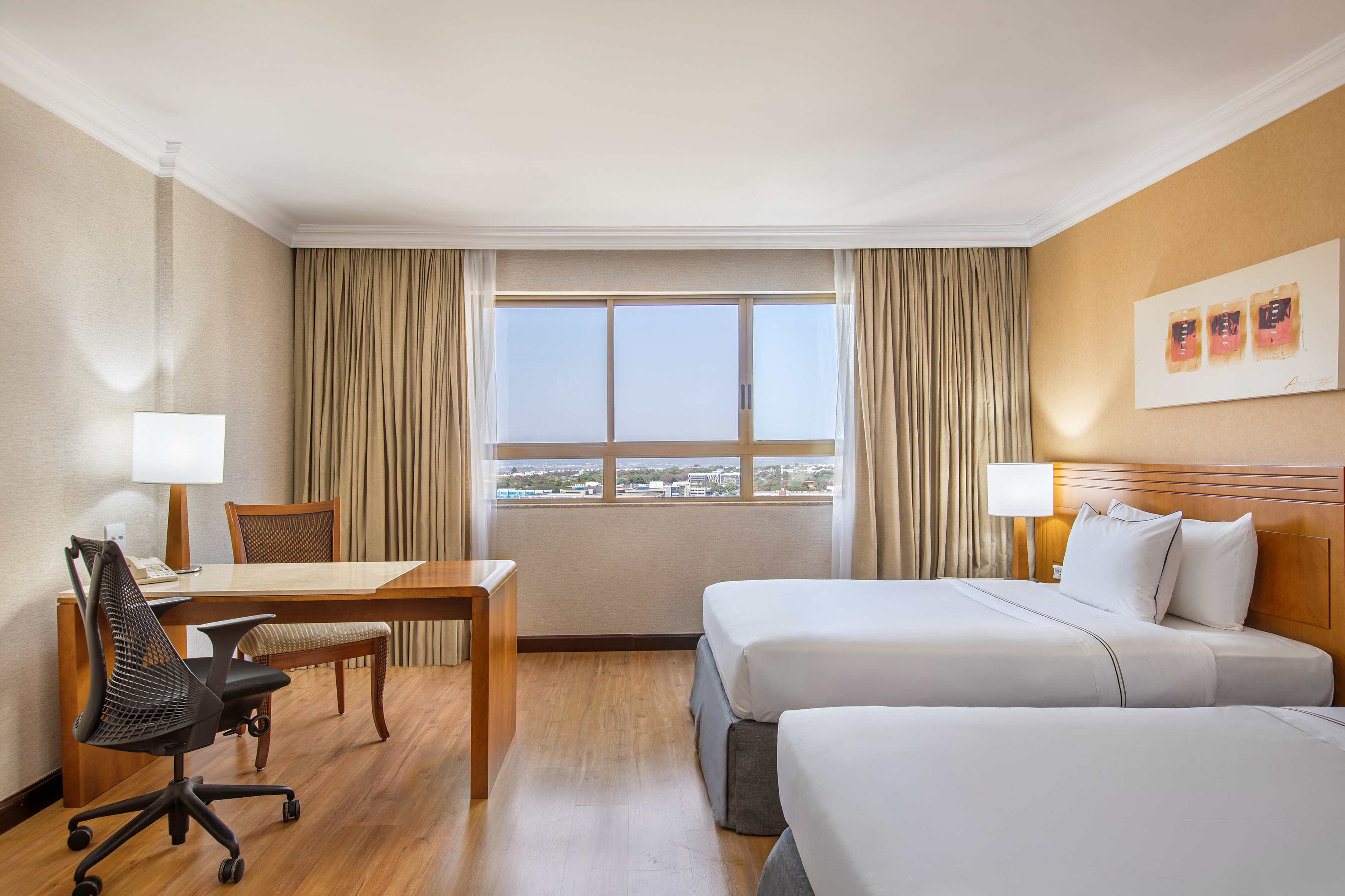 Hotel room with two twin beds, desk, and window overlooking city.