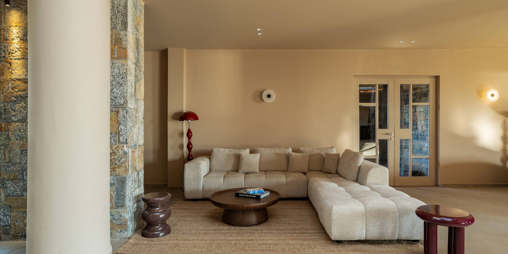 Modern beige living room with L-shaped sofa, round coffee table, stone wall.