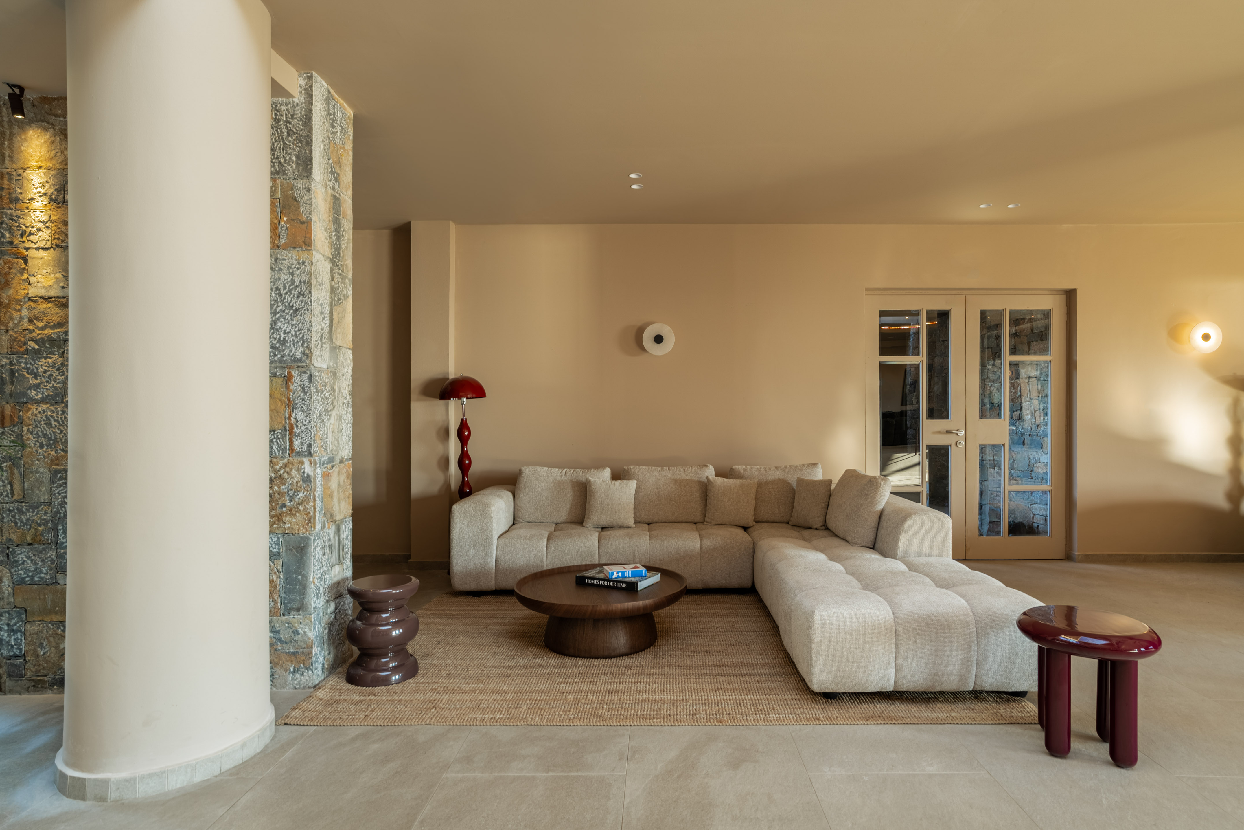 Modern beige living room with L-shaped sofa, round coffee table, stone wall.