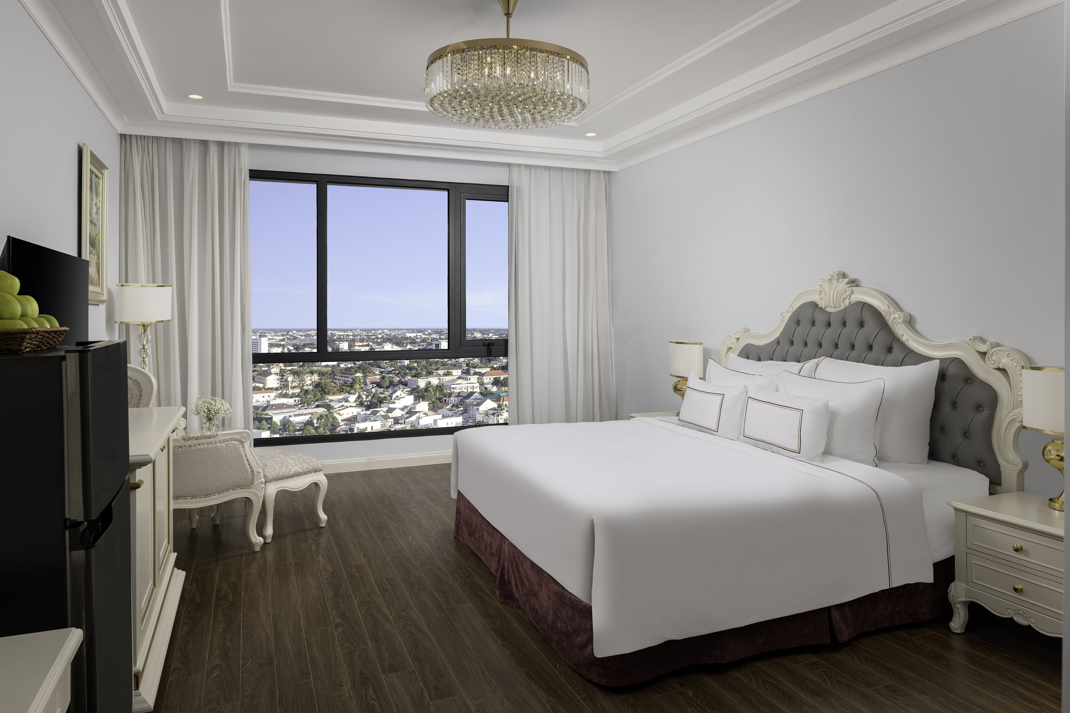 Luxury hotel bedroom with city view, king bed, elegant chandelier, and wood floor.