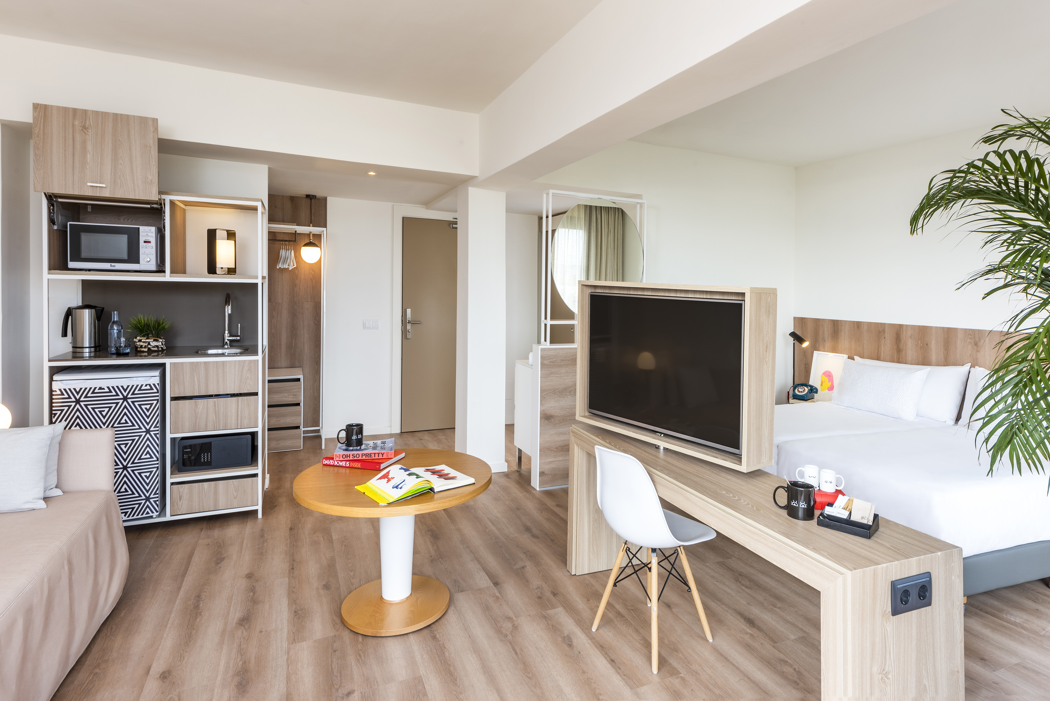 Compact hotel studio apartment with kitchenette, bed, TV, and sitting area.