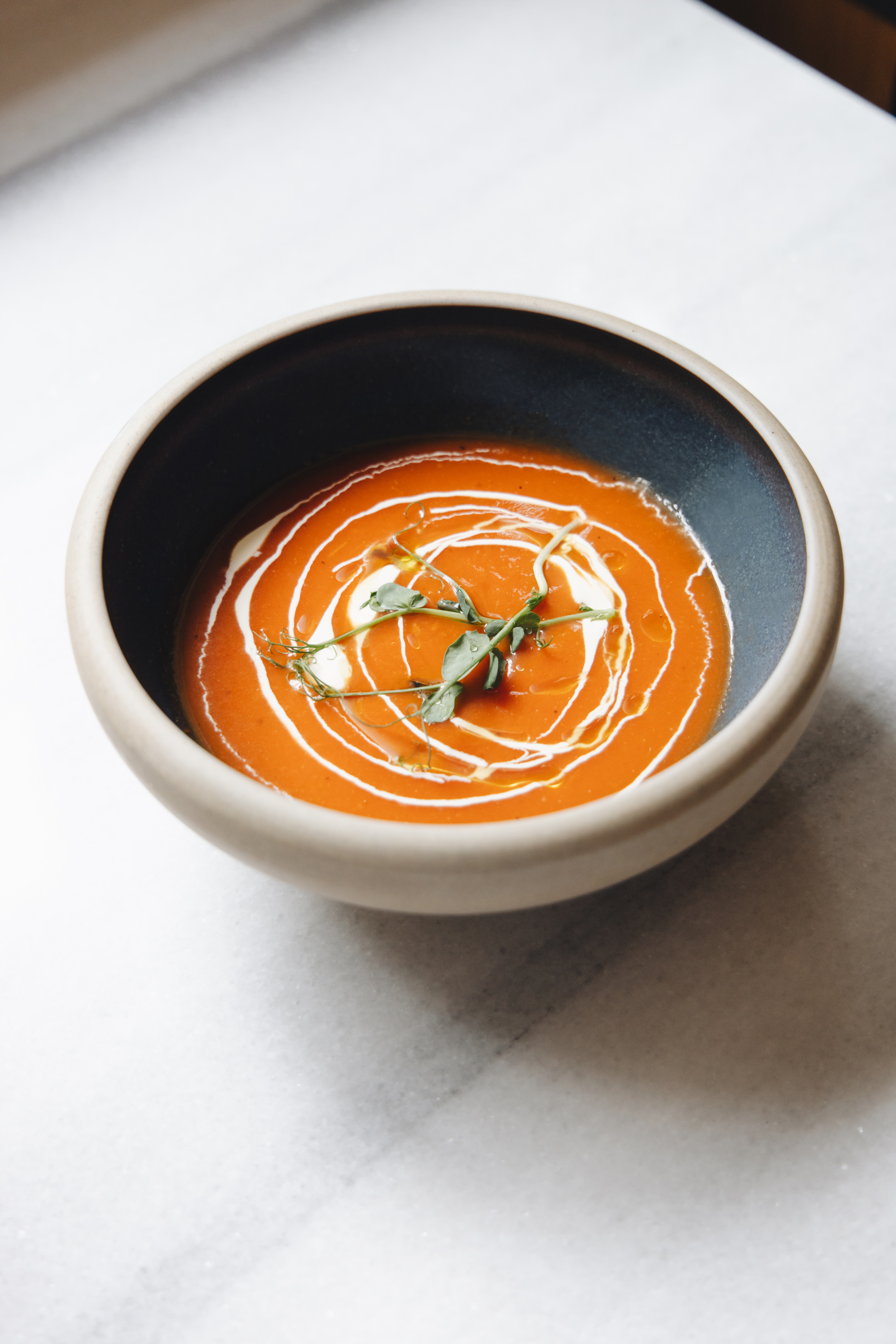 Vibrant tomato soup with cream swirl and fresh microgreens in a ceramic bowl.