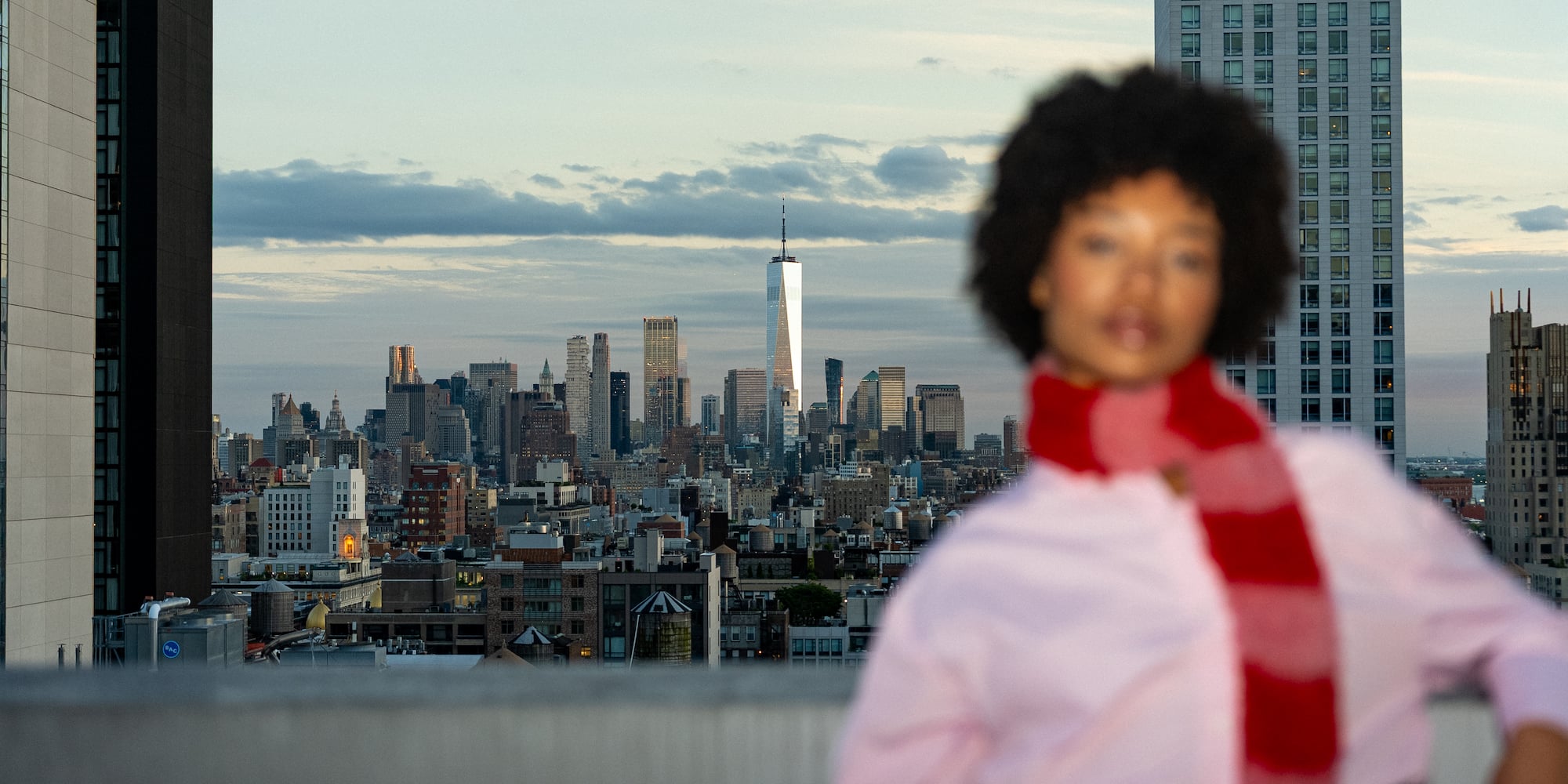 New York City skyline with One World Trade Center, blurred woman, red scarf.