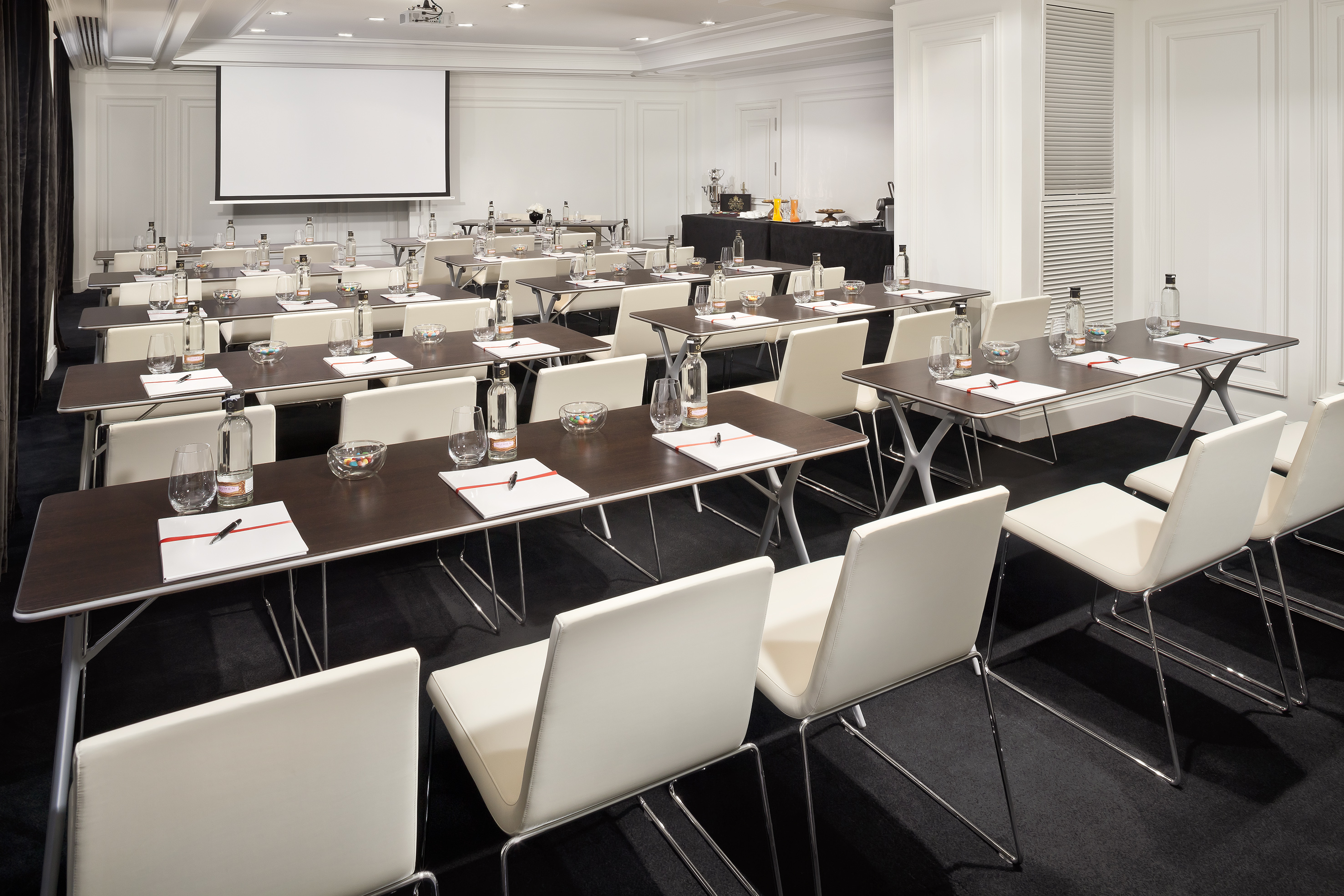 Classroom-style conference room with tables, white chairs, and projector screen.