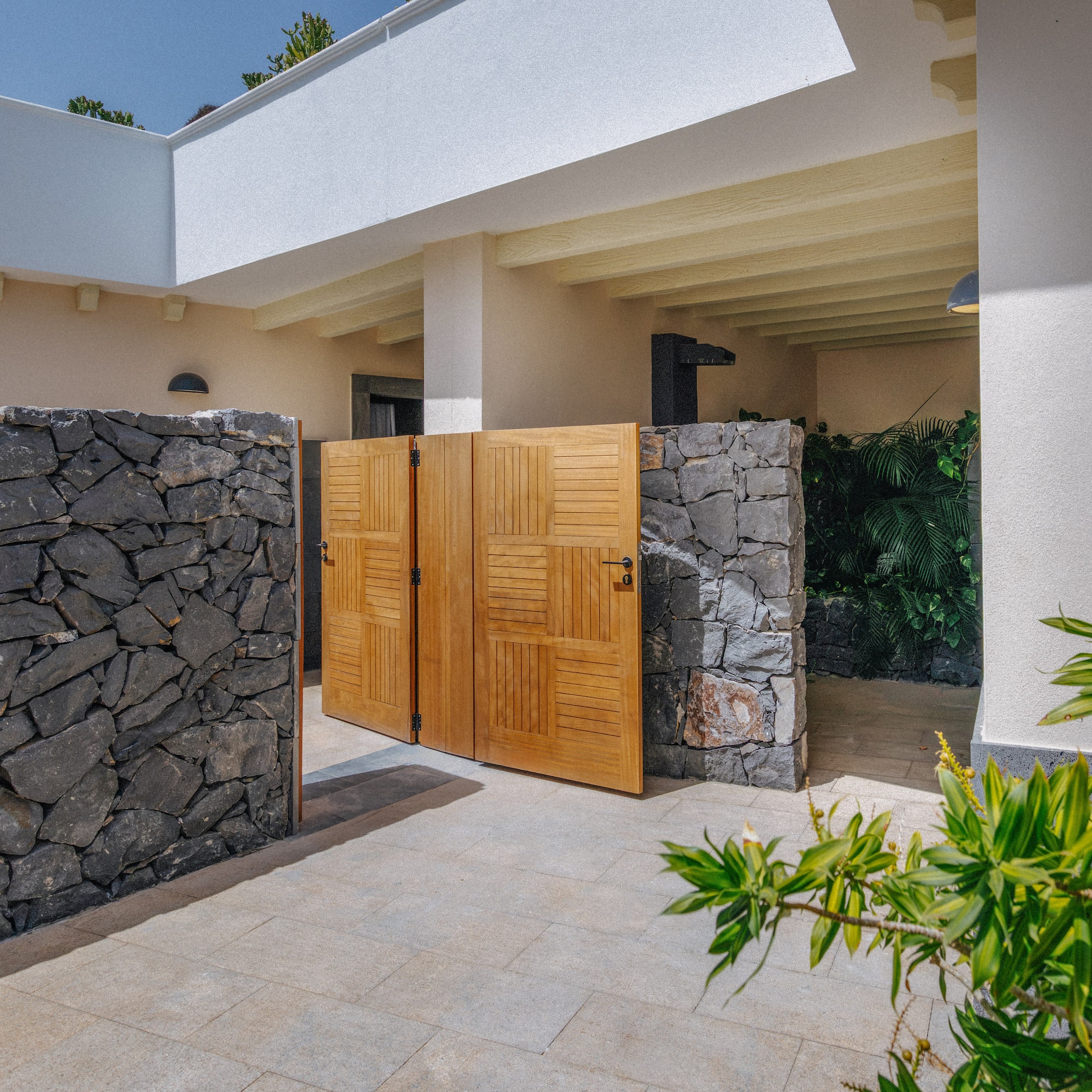 Stone wall and open wooden gate leading to a bright modern villa entrance.