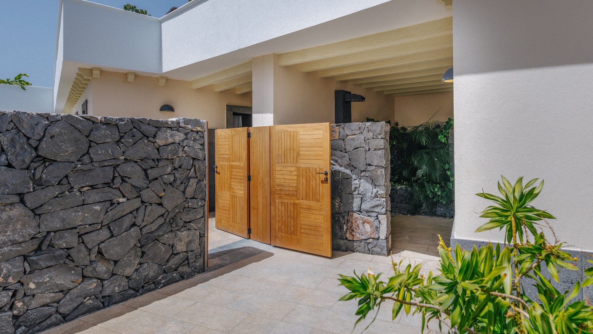 Stone wall and open wooden gate leading to a bright modern villa entrance.