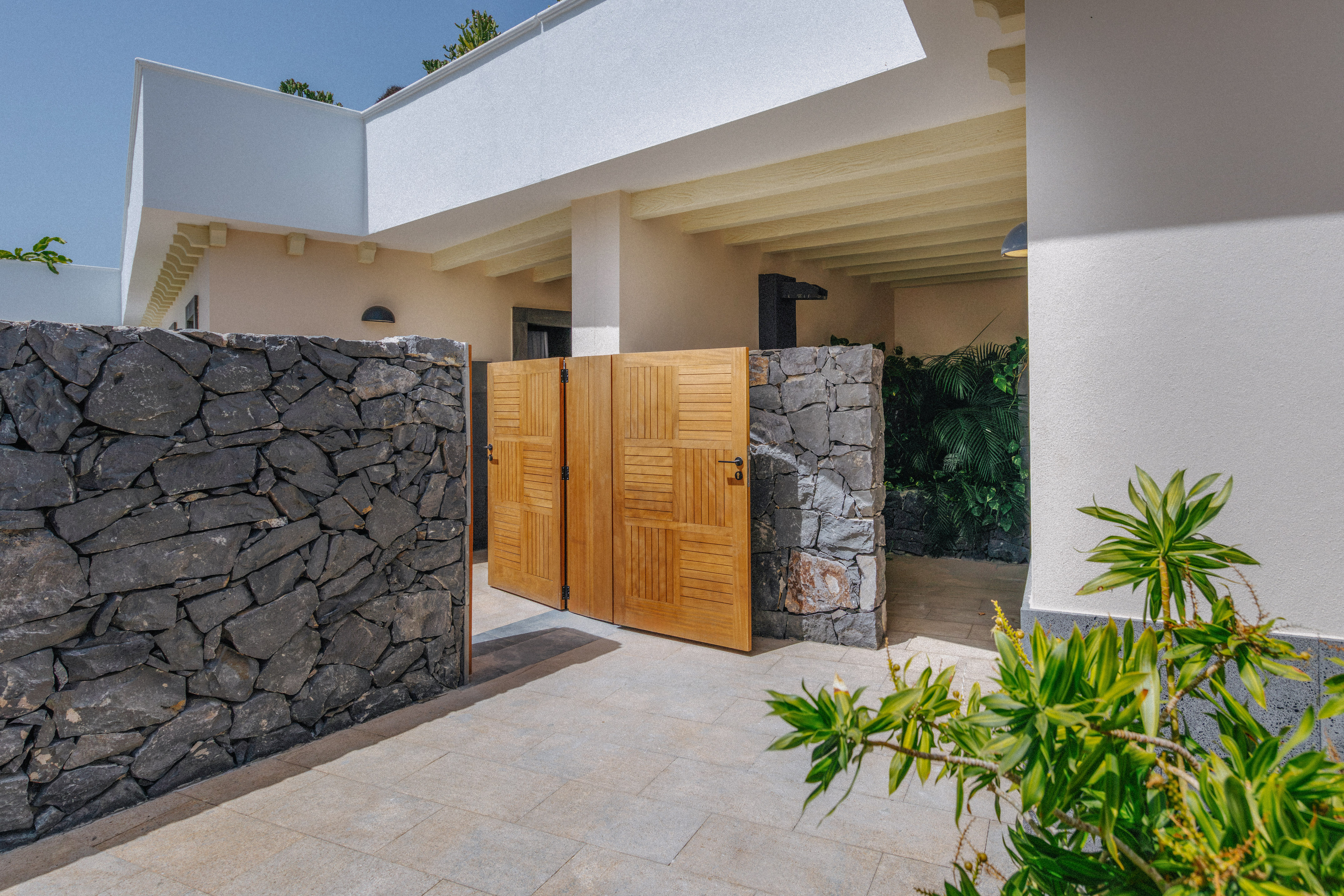 Stone wall and open wooden gate leading to a bright modern villa entrance.