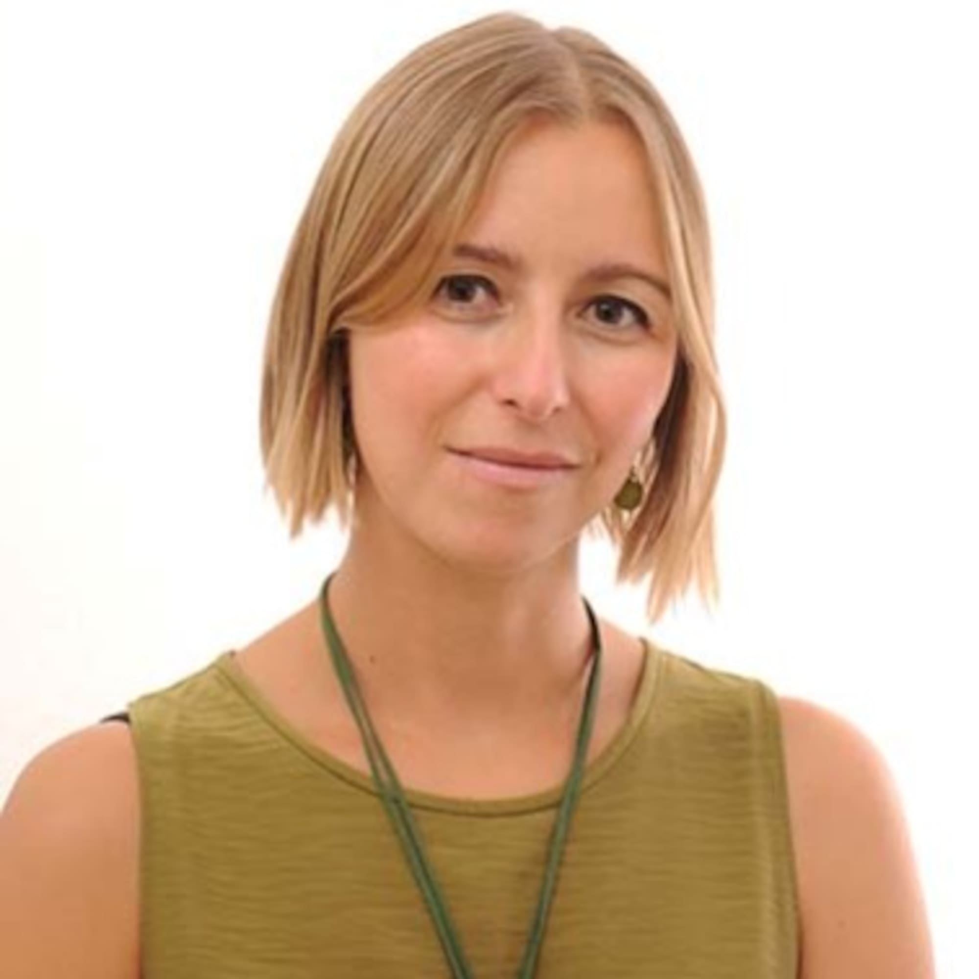 Professional headshot: blonde woman in olive green top with subtle smile.
