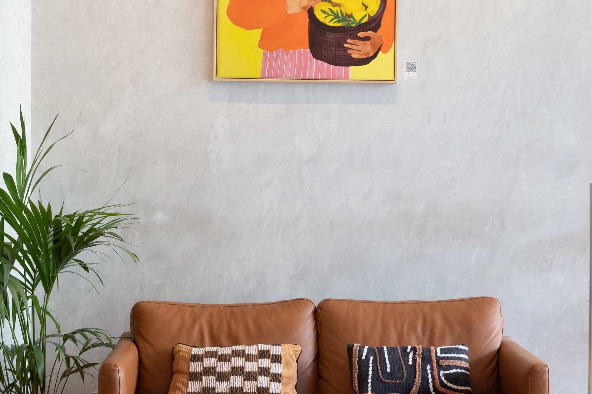 Modern living room with leather sofa, abstract art, black tables, and plant.
