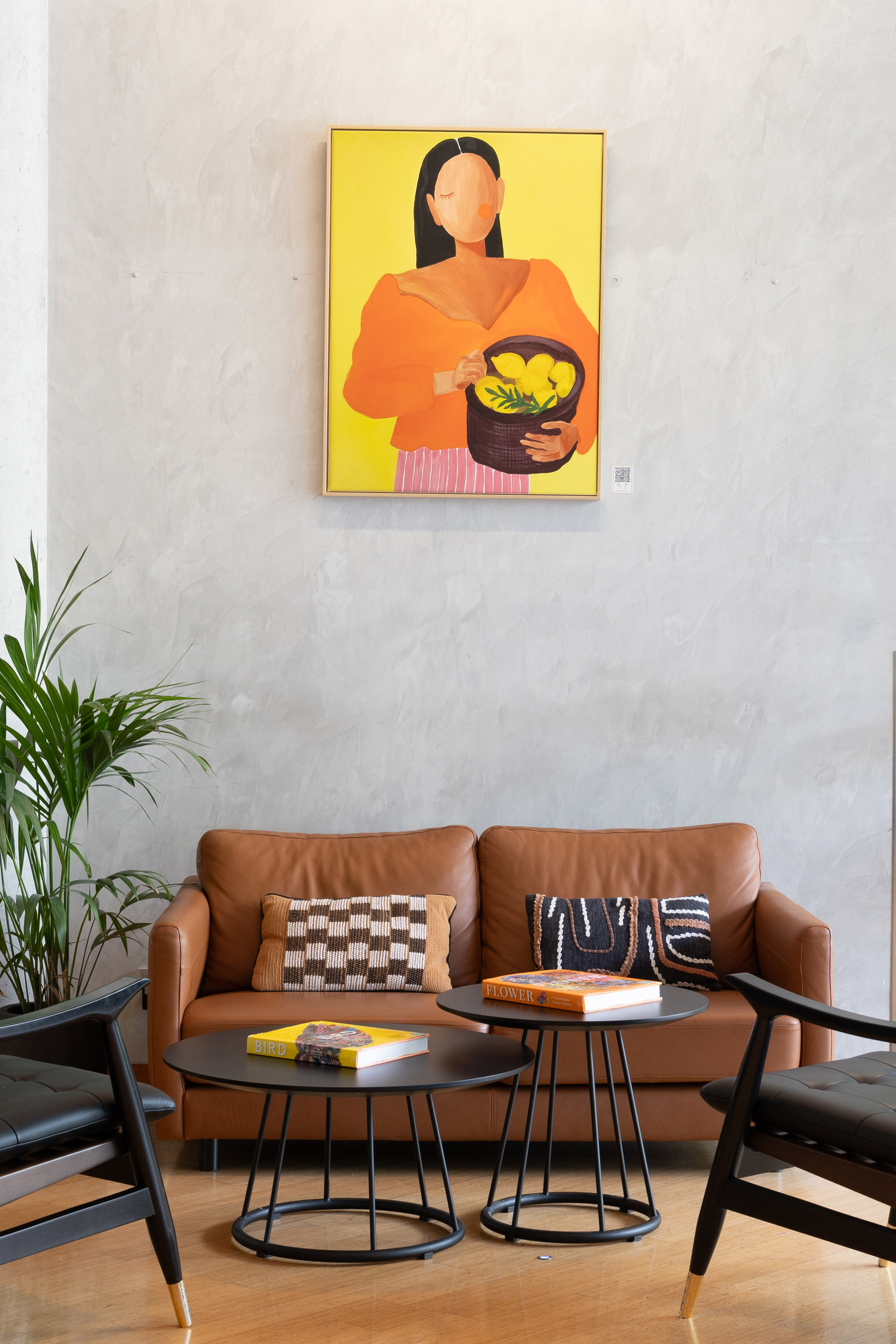 Modern living room with leather sofa, abstract art, black tables, and plant.