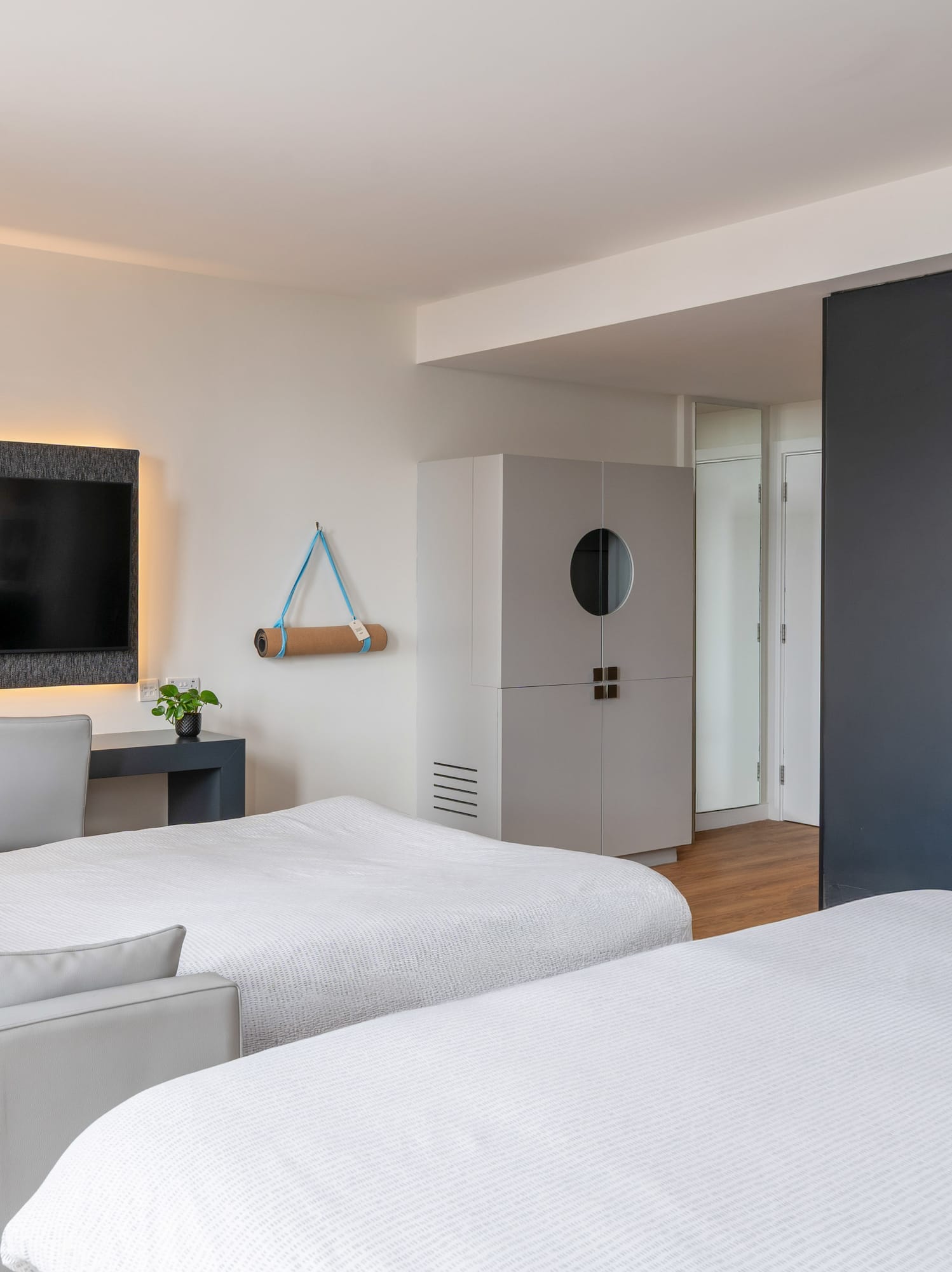 Modern hotel room with two beds, sofa, desk, backlit TV, yoga mat, and vanity.