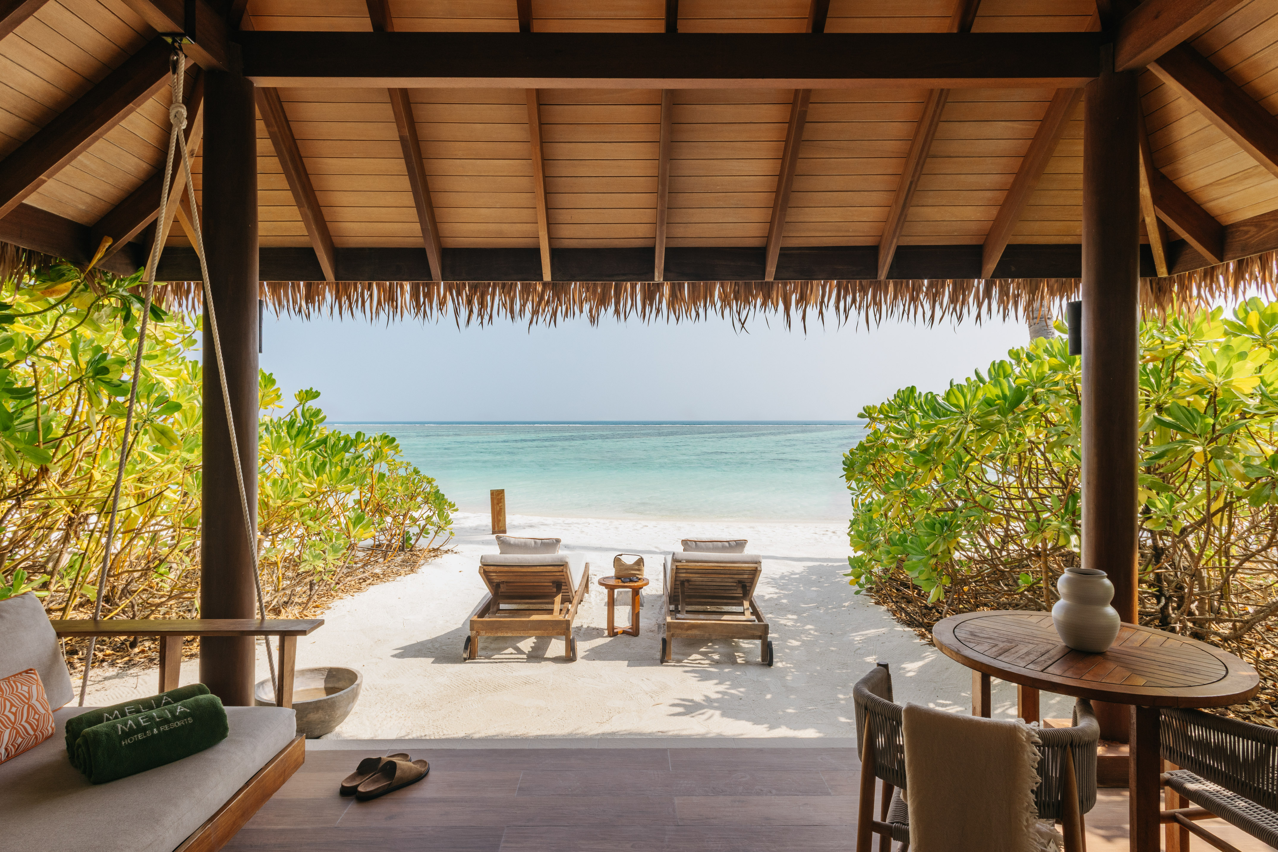 Tropical resort patio, white sand beach, turquoise ocean, sun loungers.
