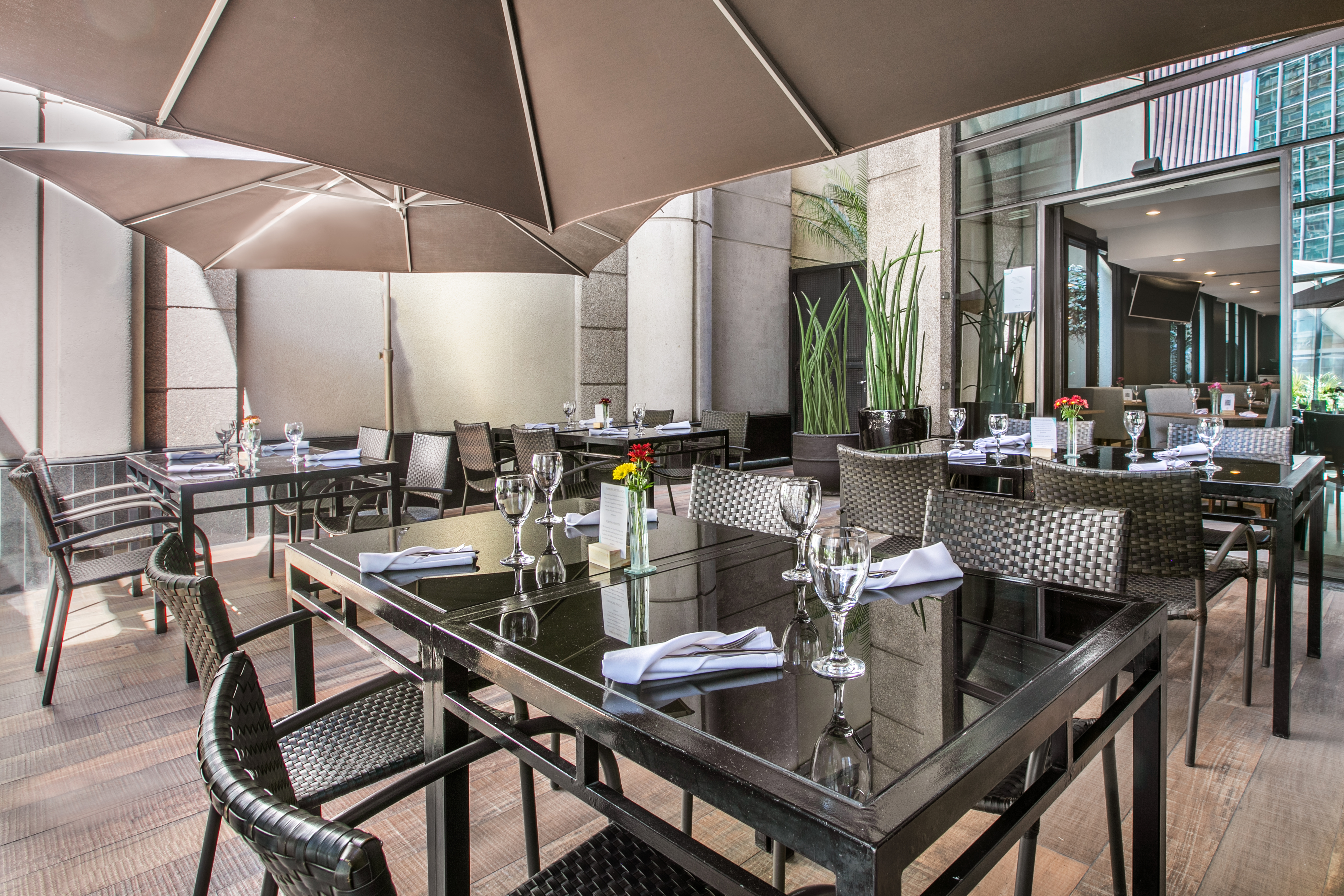 Elegant outdoor restaurant patio with set tables, chairs, and shade umbrellas.