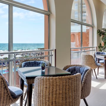 a room with a table and chairs and a balcony overlooking the ocean