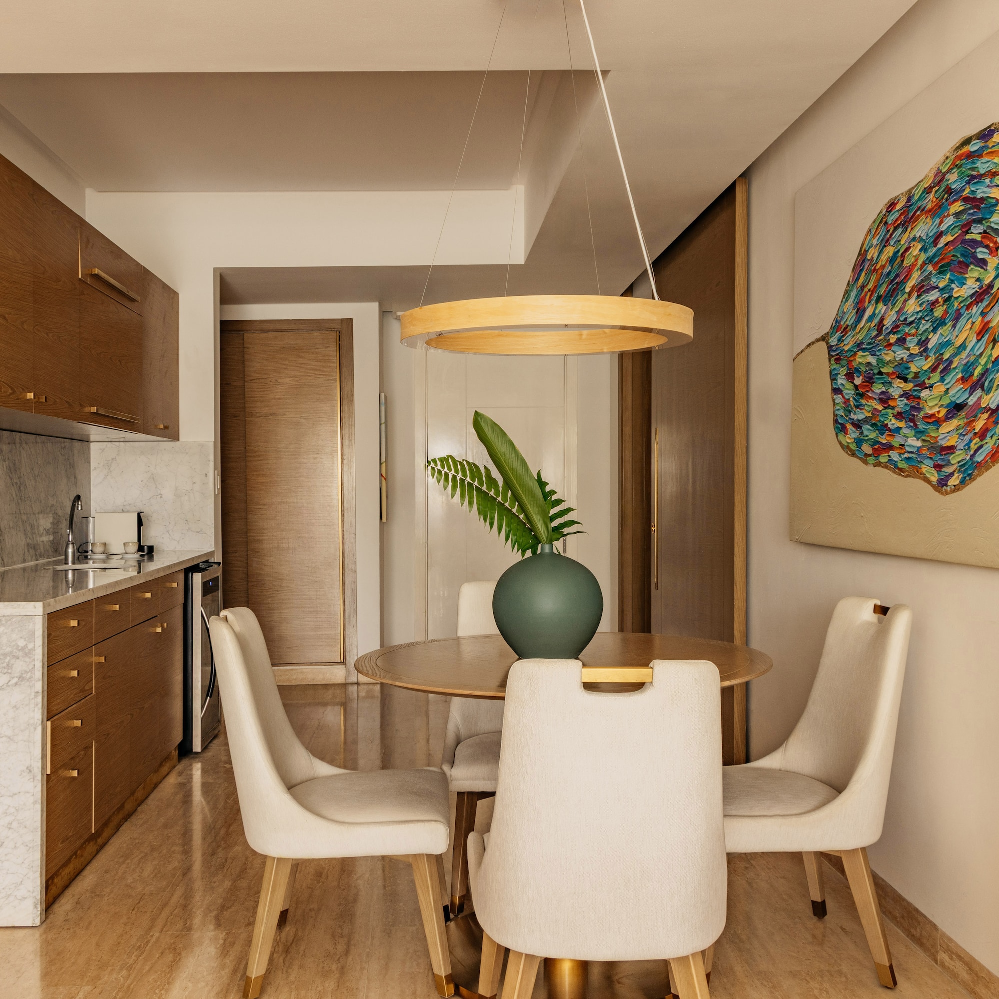Modern kitchenette, dining area with wood cabinets, marble, abstract art.