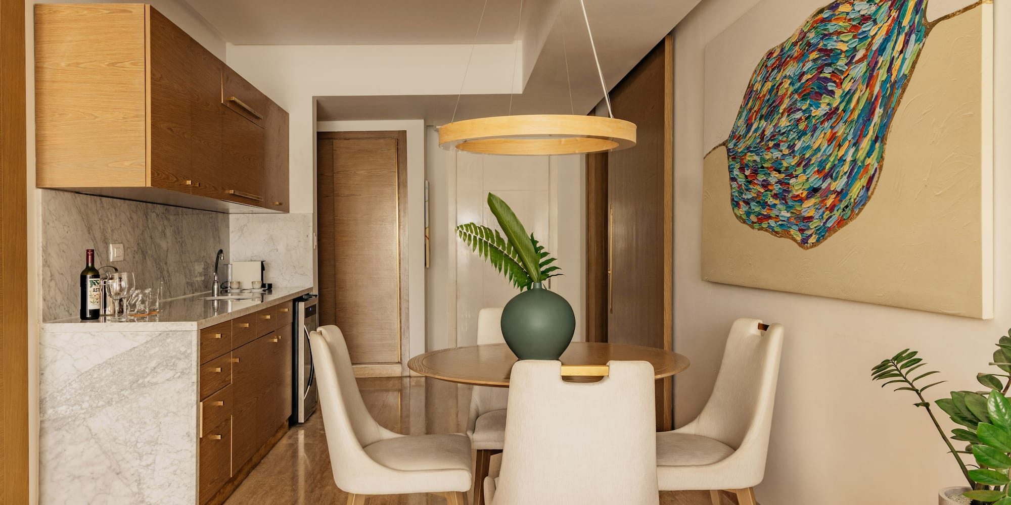 Modern kitchen & dining area: wood cabinets, marble, round table, abstract art.