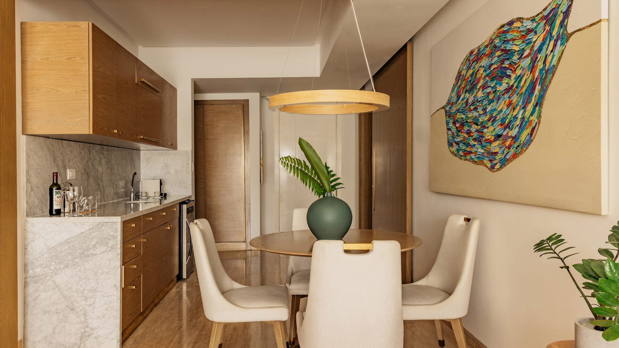 Modern kitchenette, dining area with wood cabinets, marble, abstract art.