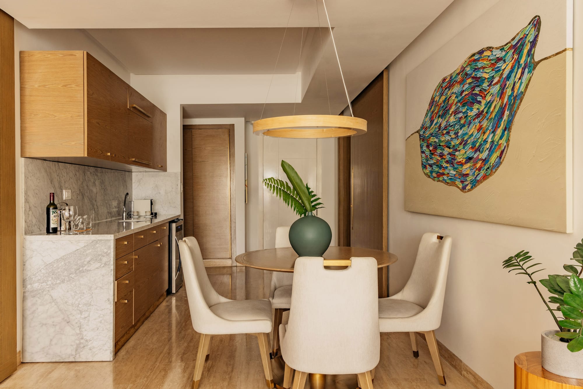 Modern kitchenette, dining area with wood cabinets, marble, abstract art.