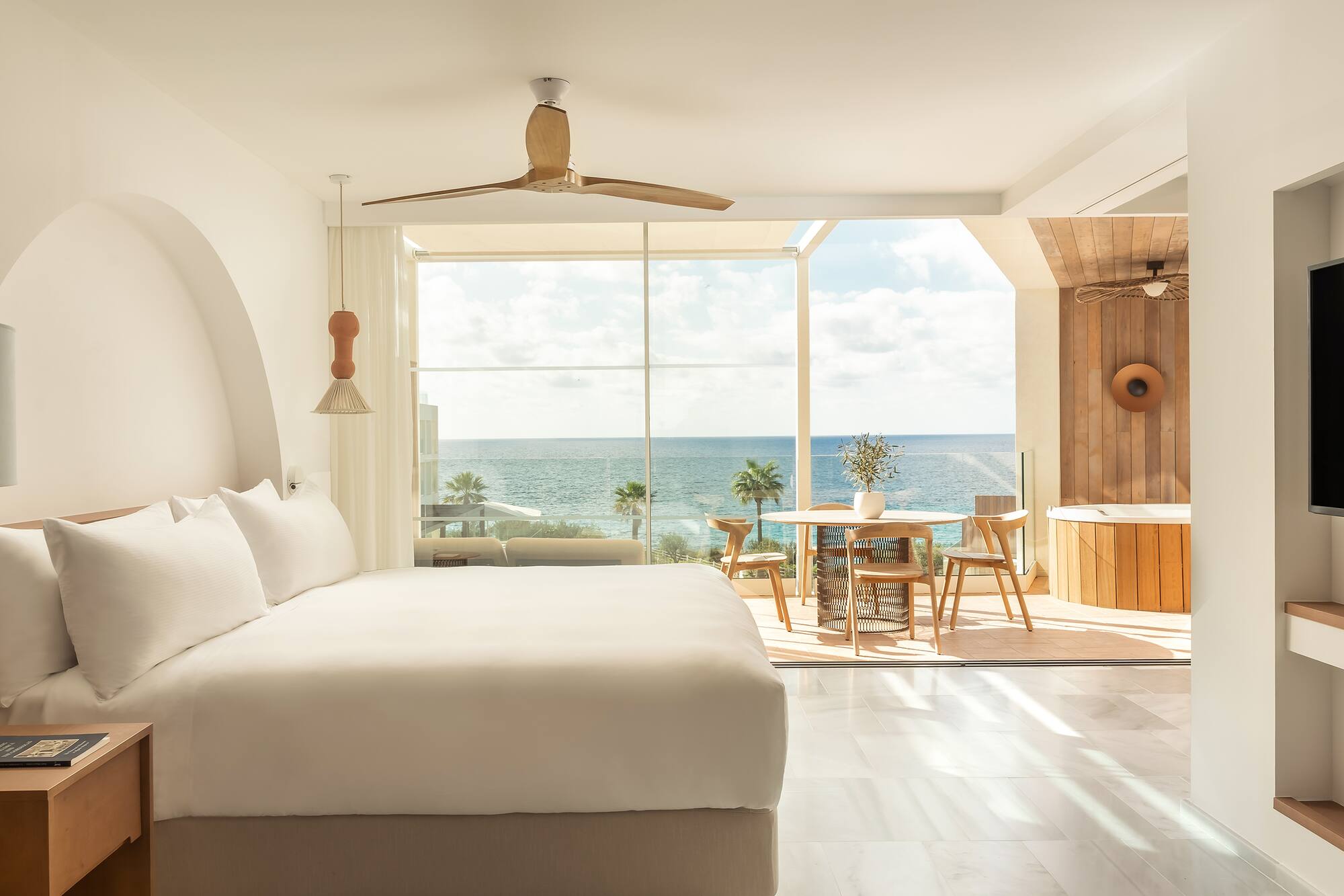 Bright oceanfront luxury suite with bed, balcony, and outdoor hot tub.