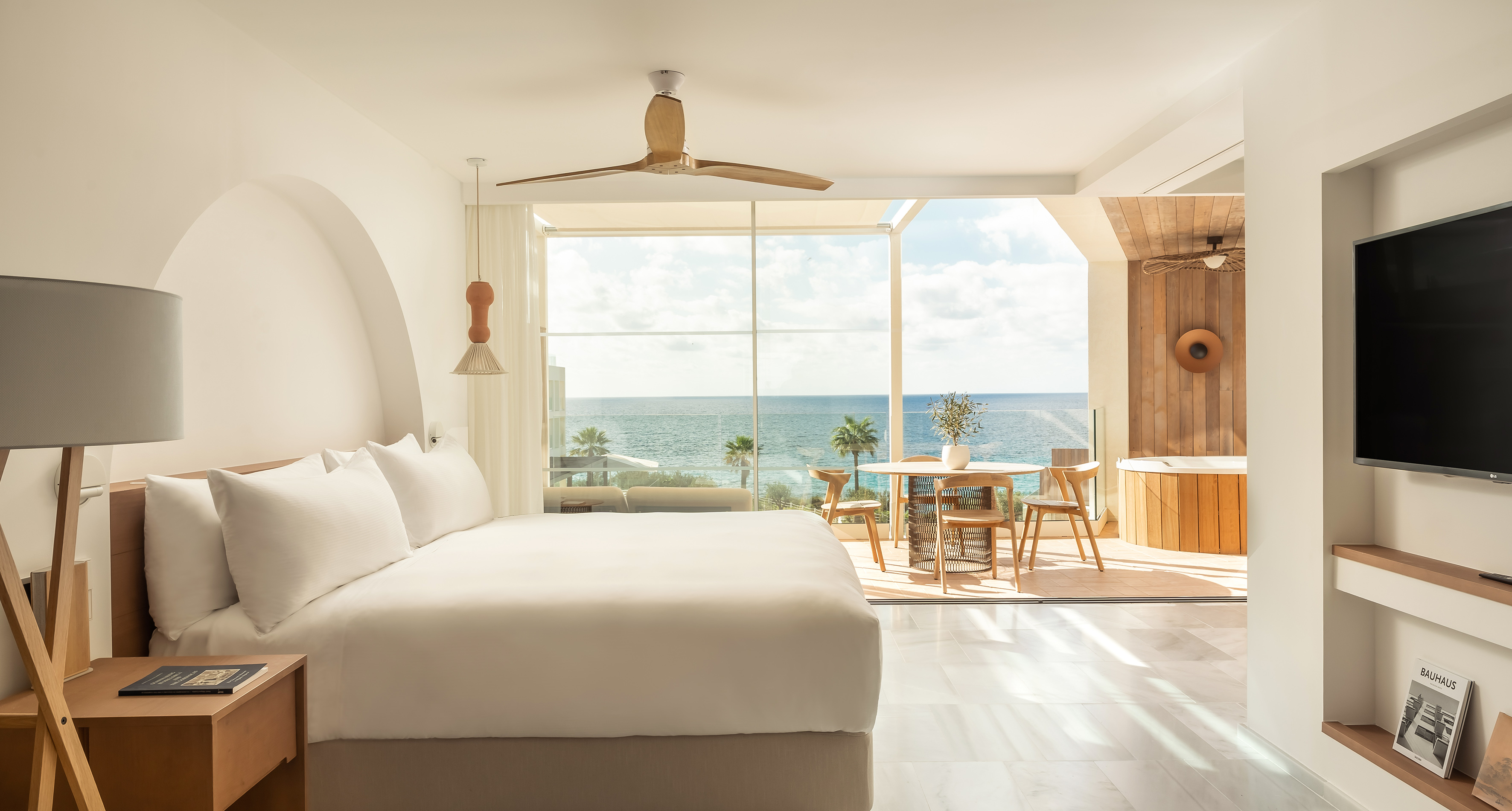 Bright oceanfront luxury suite with bed, balcony, and outdoor hot tub.