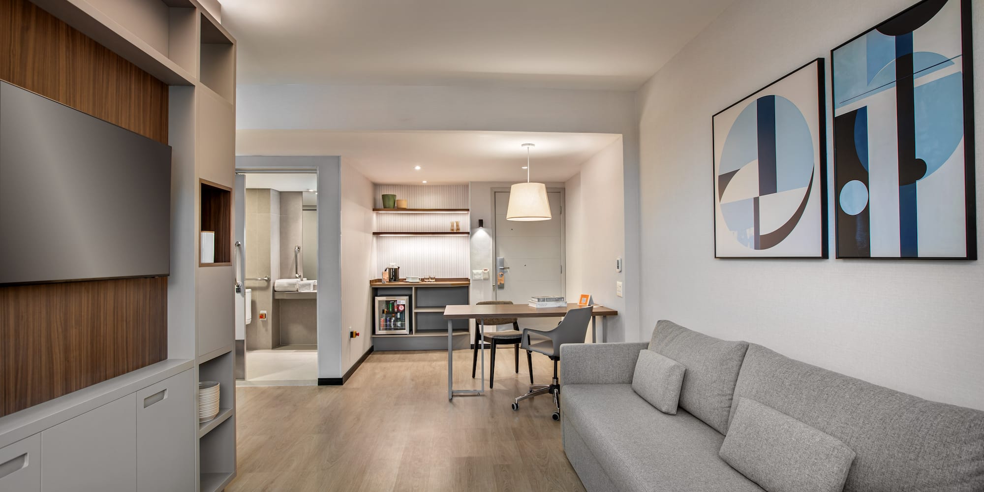 Stylish studio apartment living area with gray sofa, kitchenette, and dining desk.