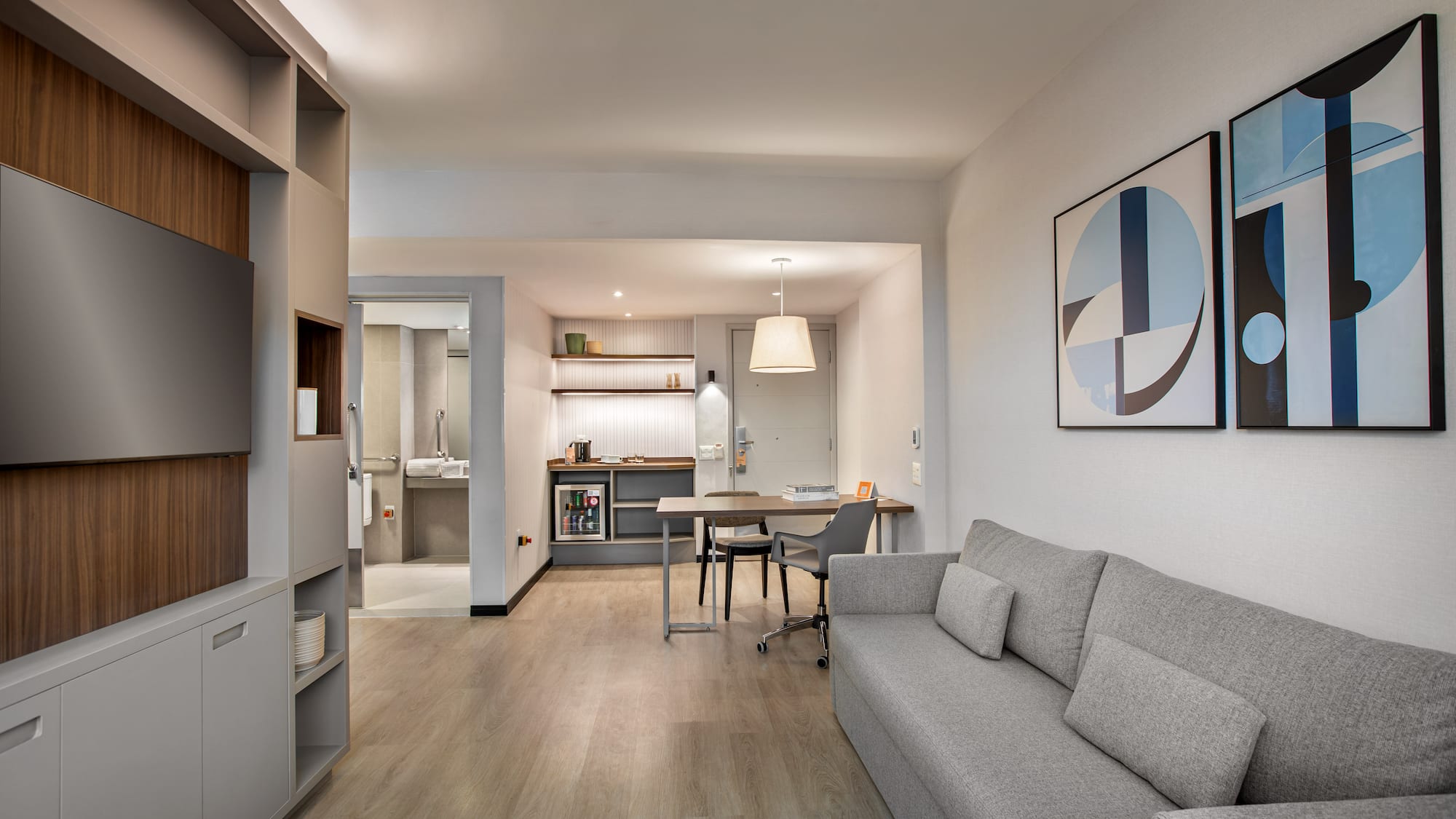 Stylish studio apartment living area with gray sofa, kitchenette, and dining desk.