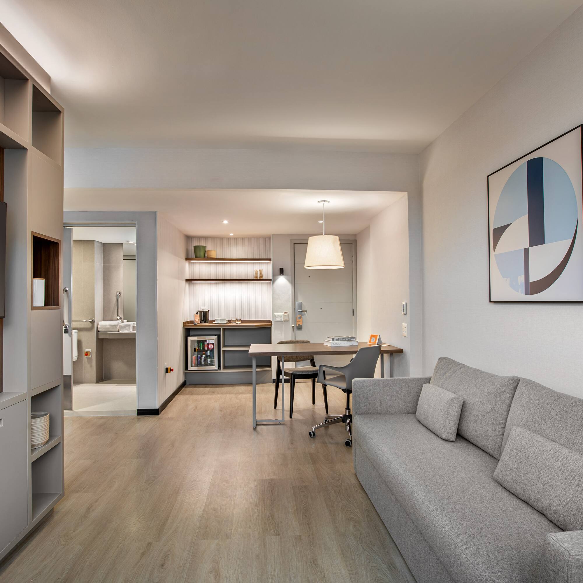 Stylish studio apartment living area with gray sofa, kitchenette, and dining desk.
