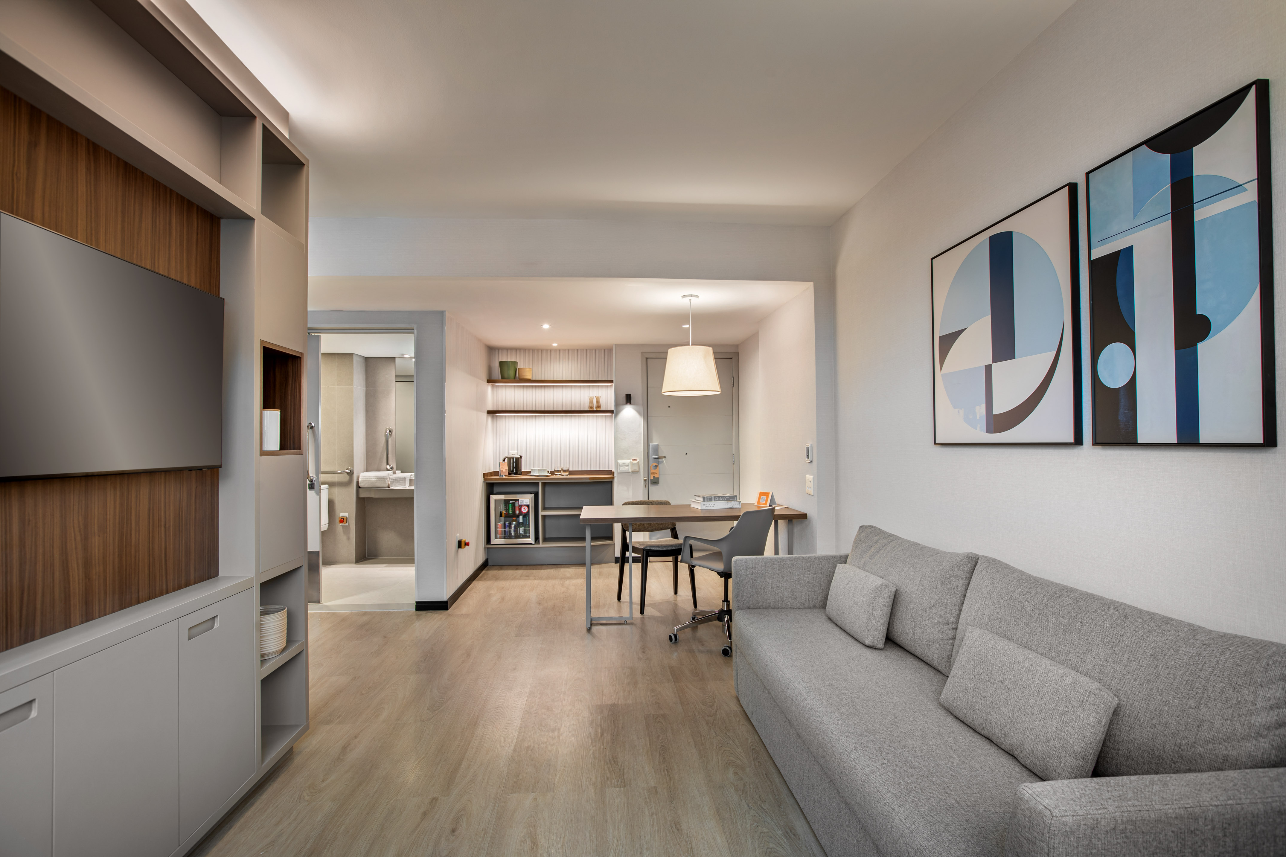Stylish studio apartment living area with gray sofa, kitchenette, and dining desk.