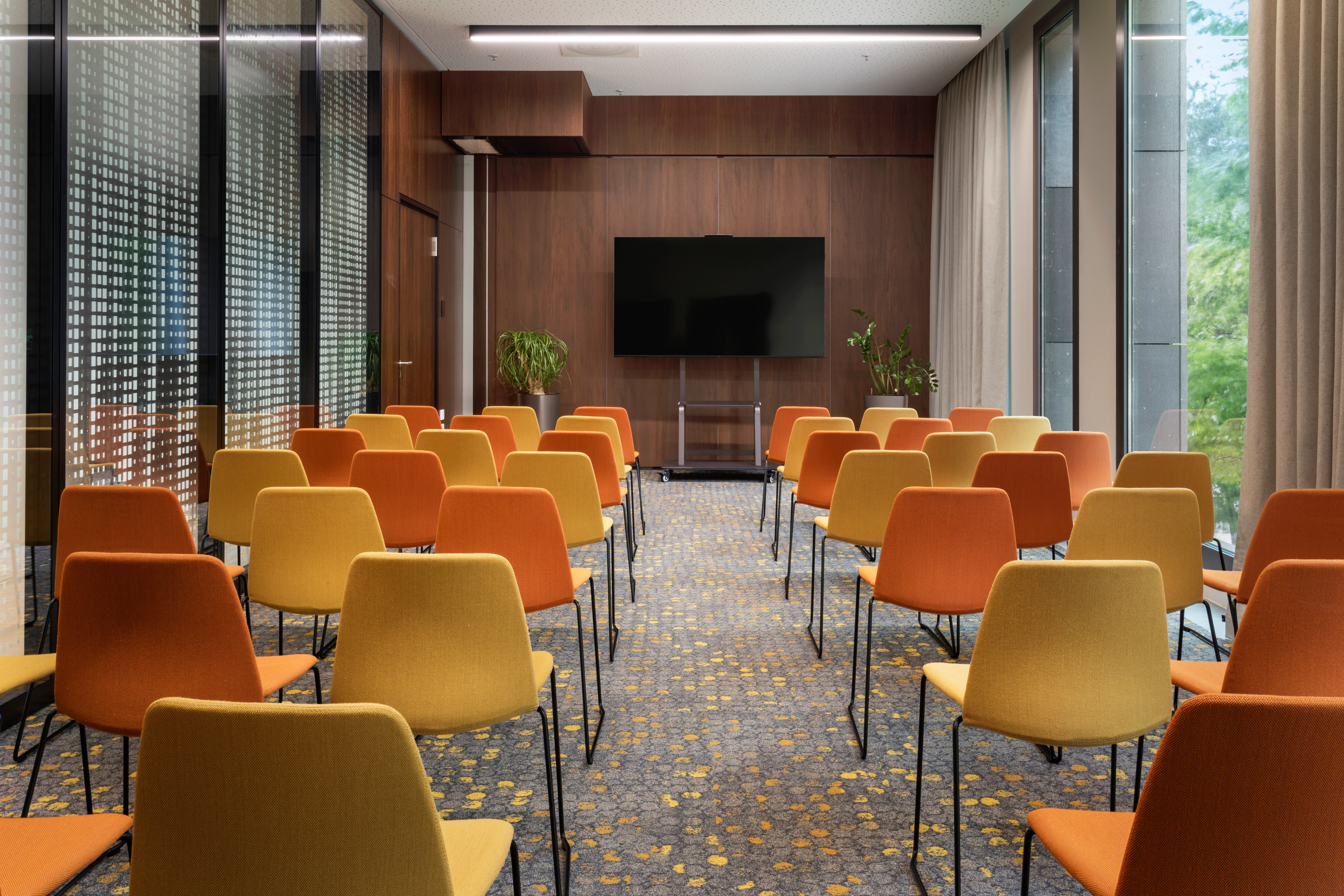 Modern conference room with orange and yellow chairs facing a large screen.