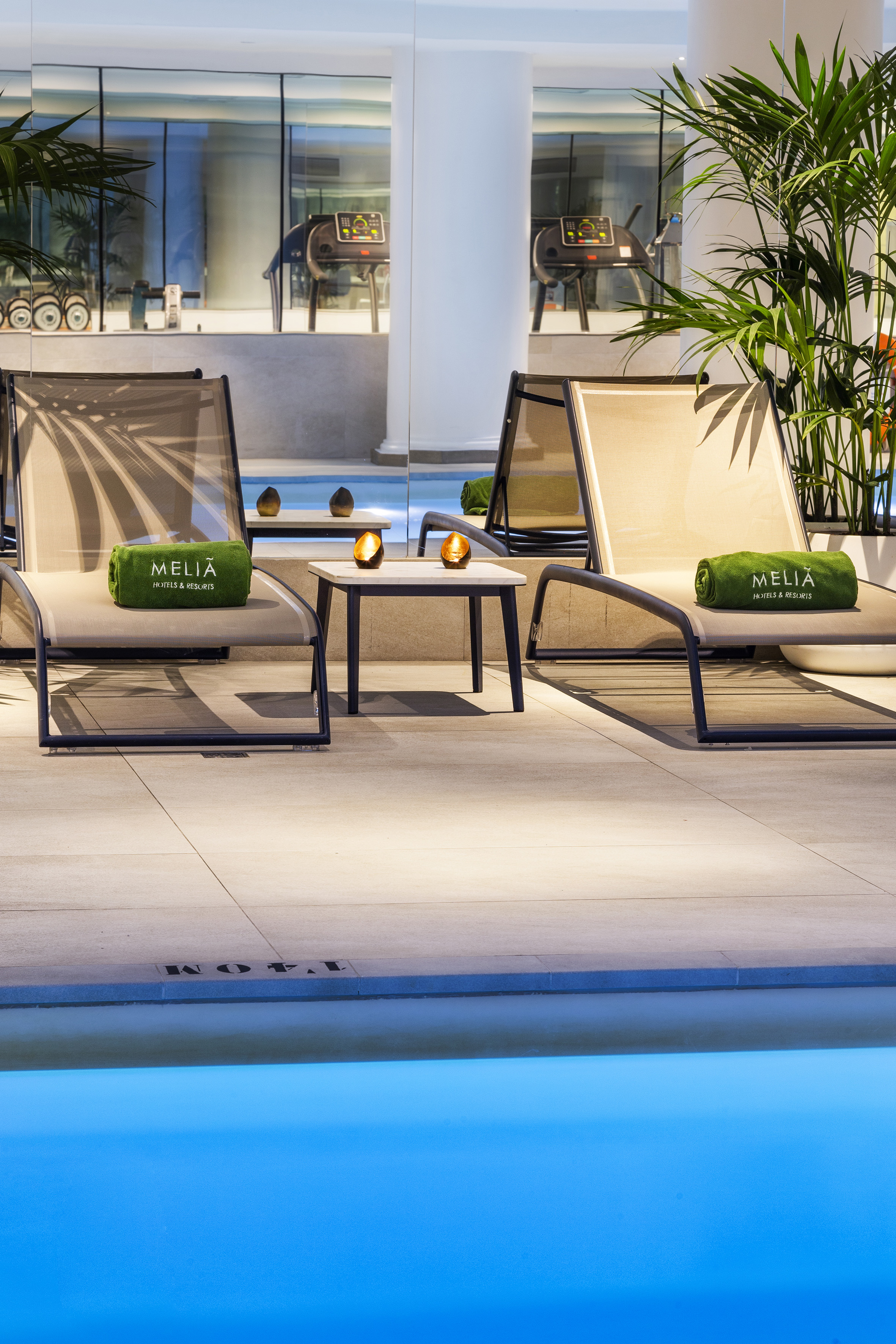 Meliá hotel pool lounge with chaises, Meliá towels, and gym reflection.