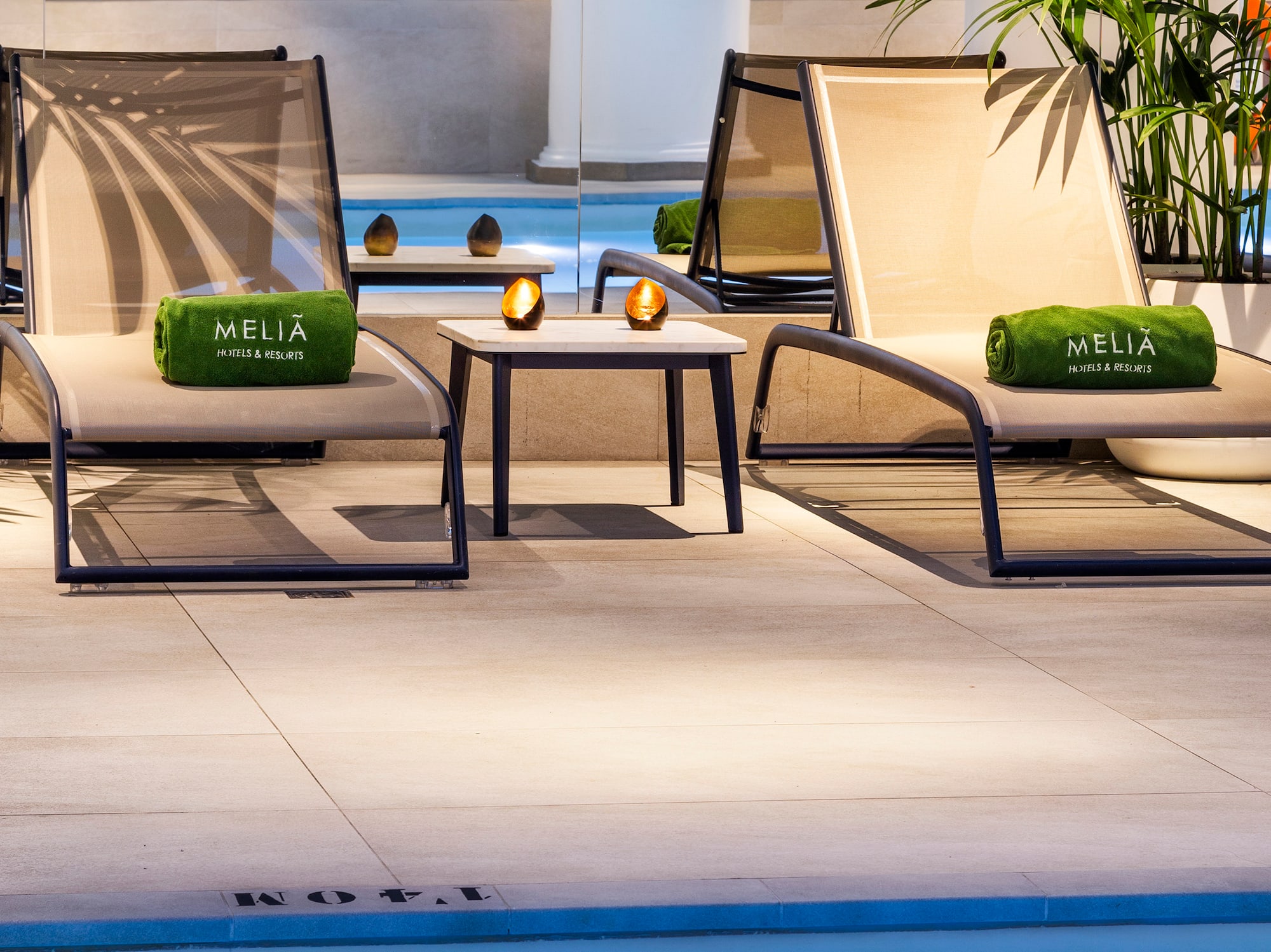 Meliá hotel pool lounge with chaises, Meliá towels, and gym reflection.
