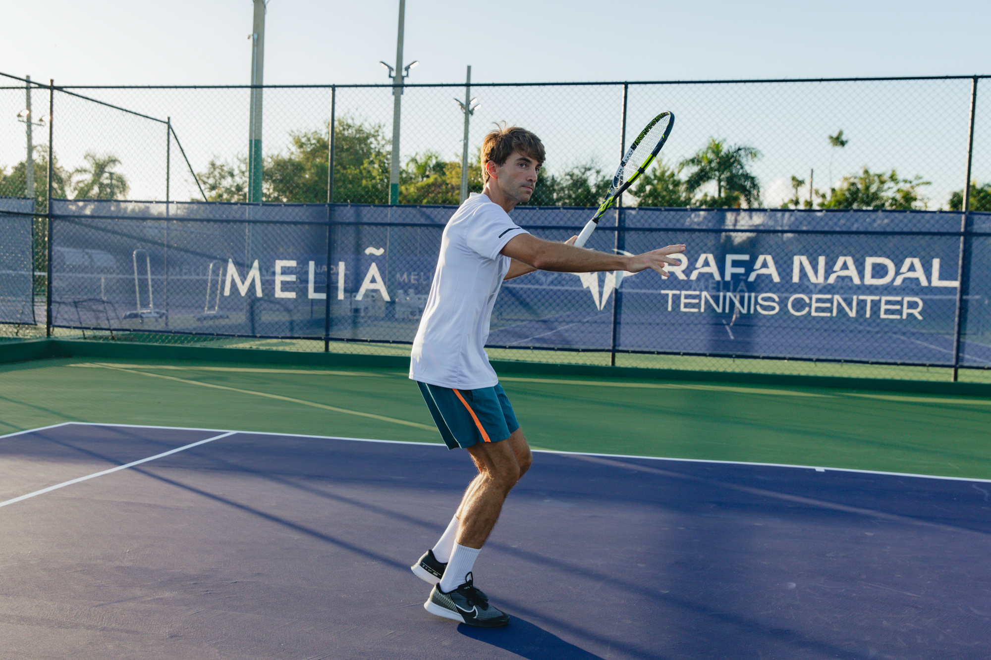 Man playing tennis on blue court at Rafa Nadal Tennis Center.