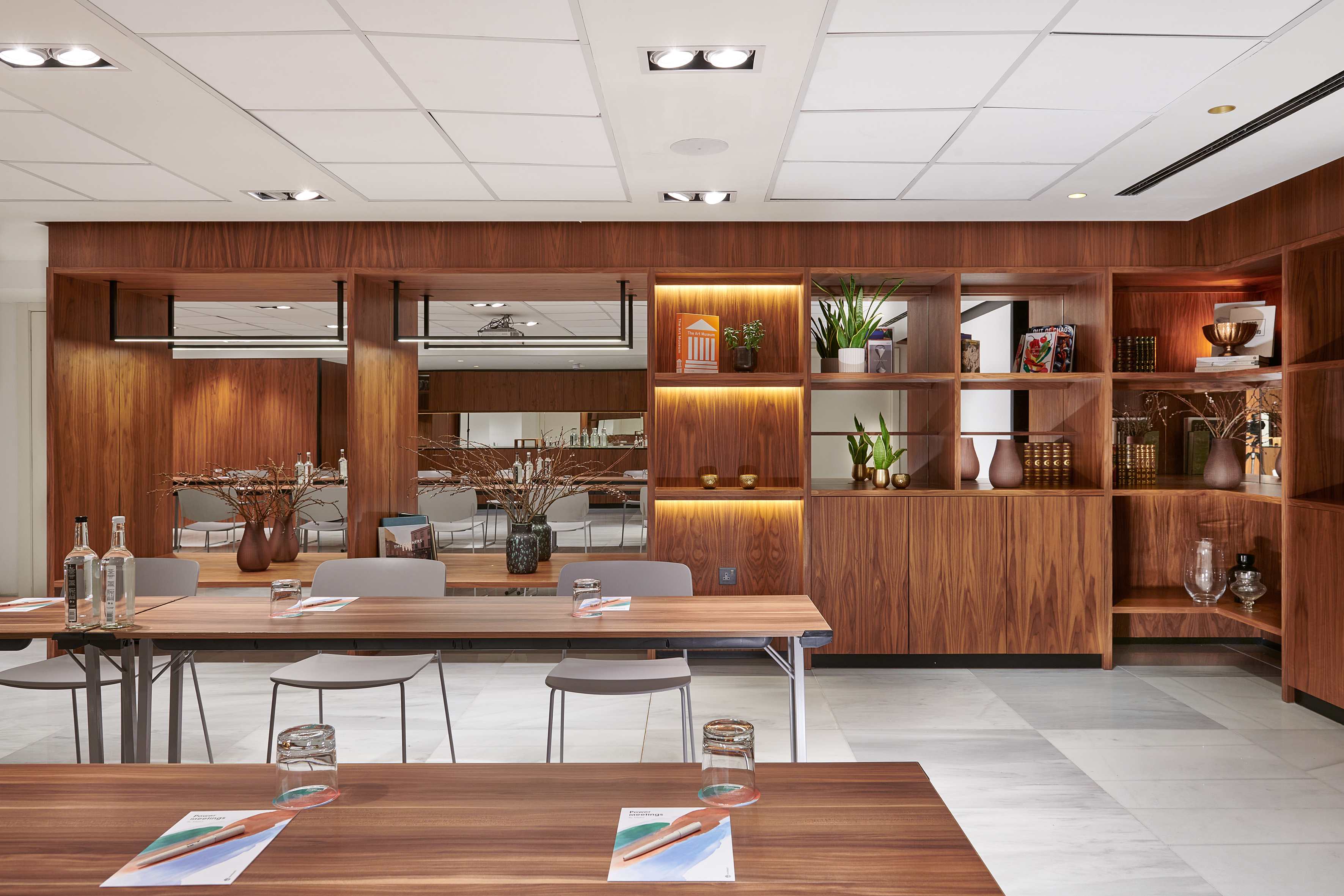 Modern meeting room with long wooden tables and illuminated shelving.