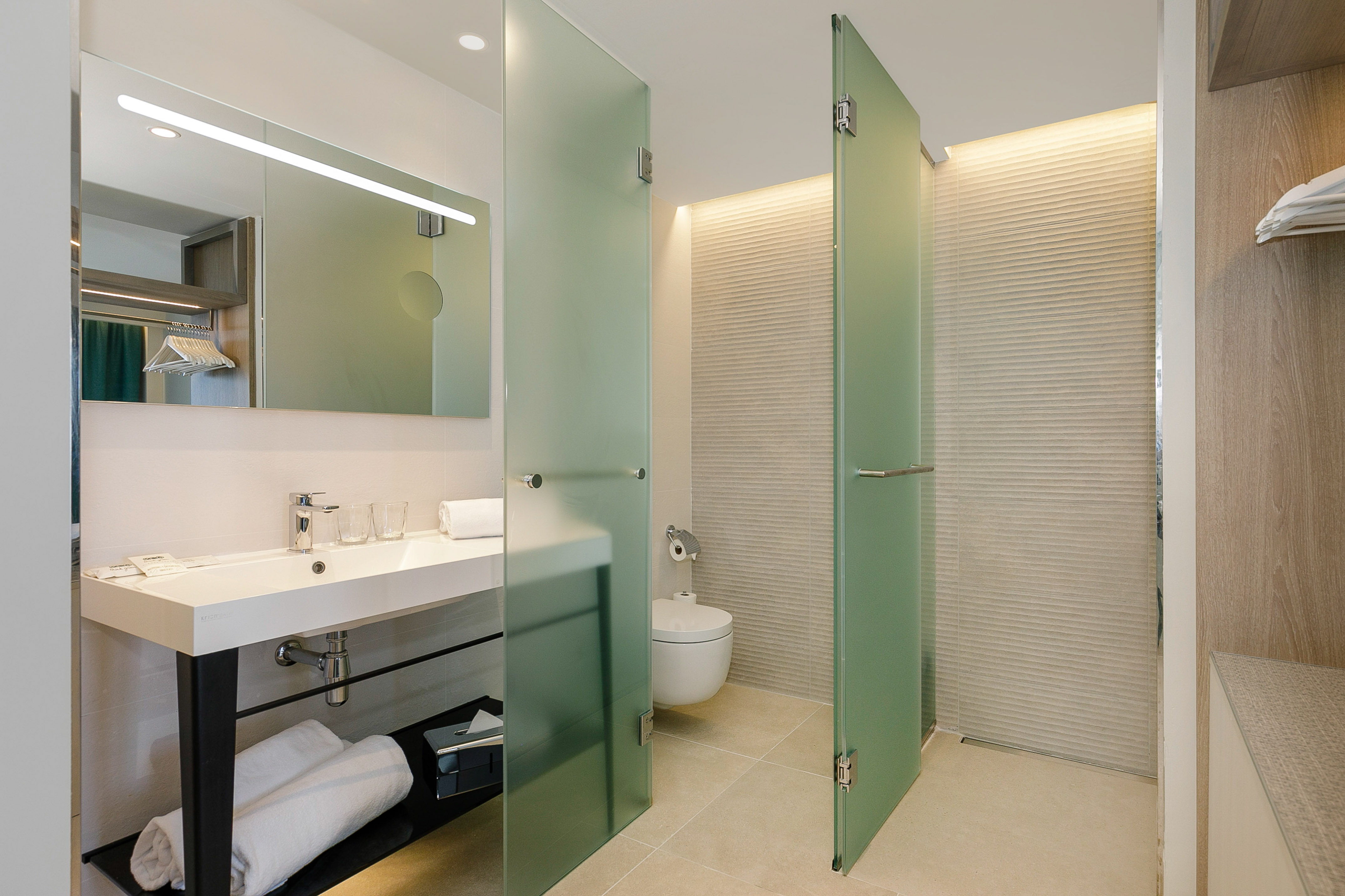 Modern bathroom with vanity, LED mirror, and frosted glass toilet/shower doors.