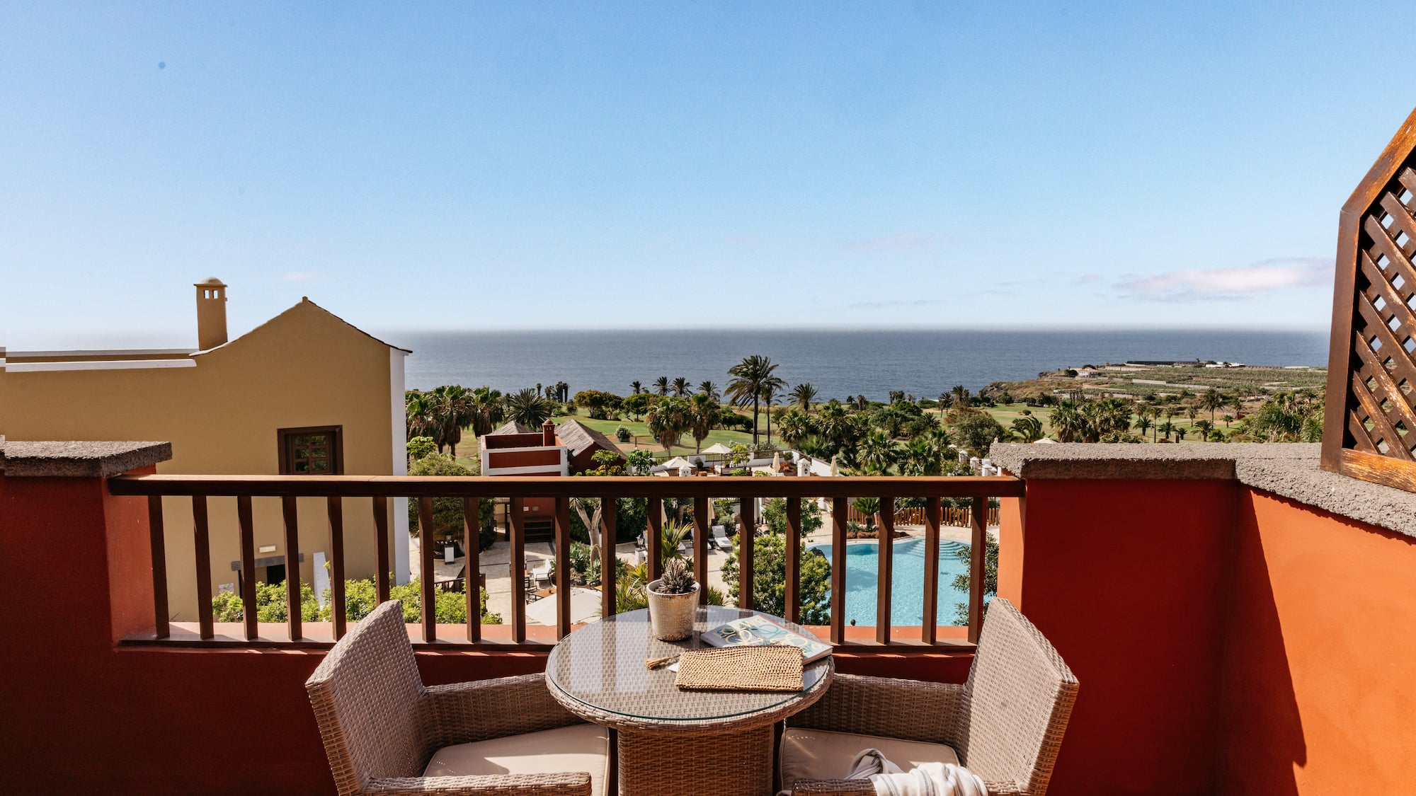Oceanfront balcony with wicker furniture, palm trees, and pool view.