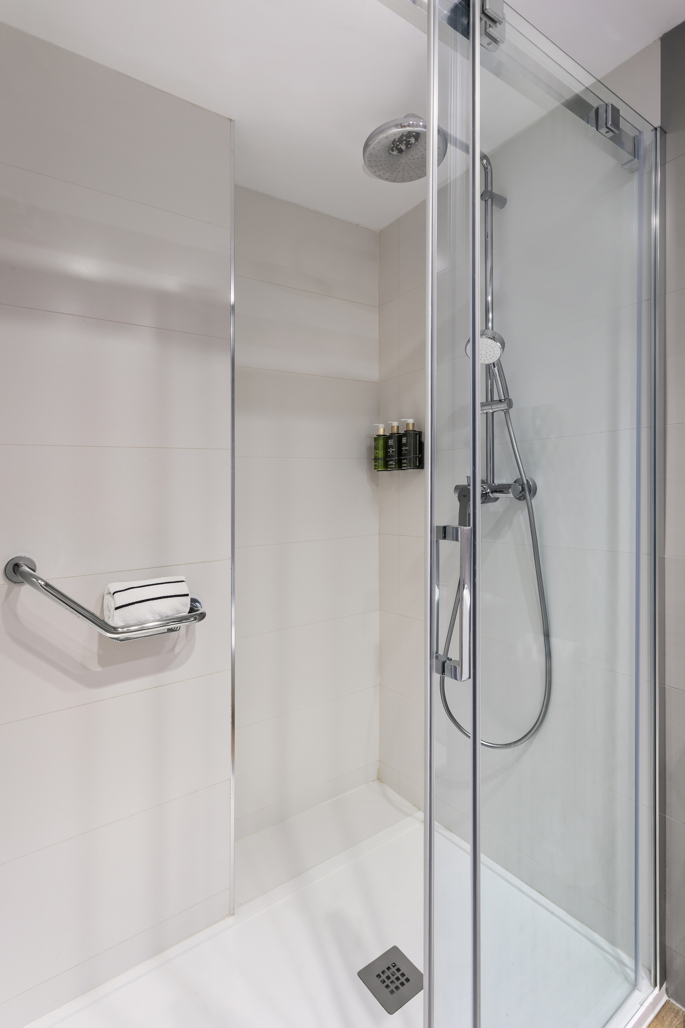 Modern shower with glass door, rain showerhead, grab bar, and toiletries.